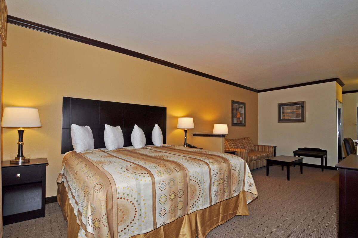 A hotel room with a large bed, two bedside lamps, a sofa, a small table, and a chair.