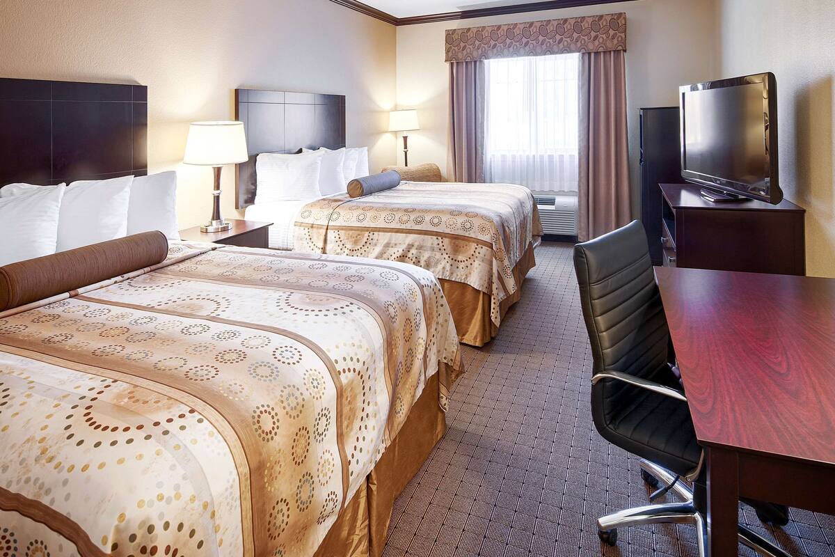 A hotel room with two beds, a desk, a chair, a television, and a window with curtains.