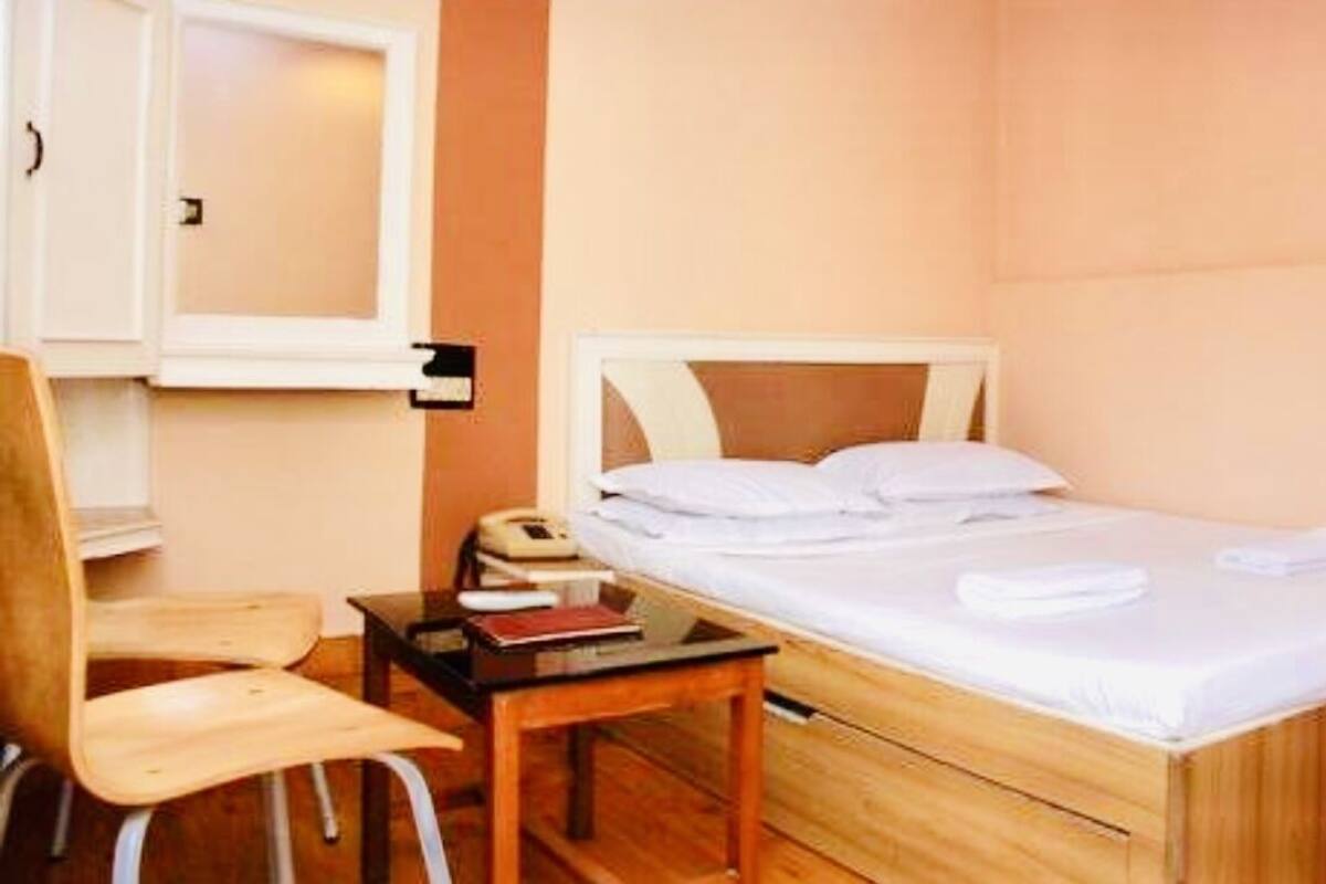 Un llit individual amb capçalera de fusta, una taula de nit amb una làmpada, i una cadira.