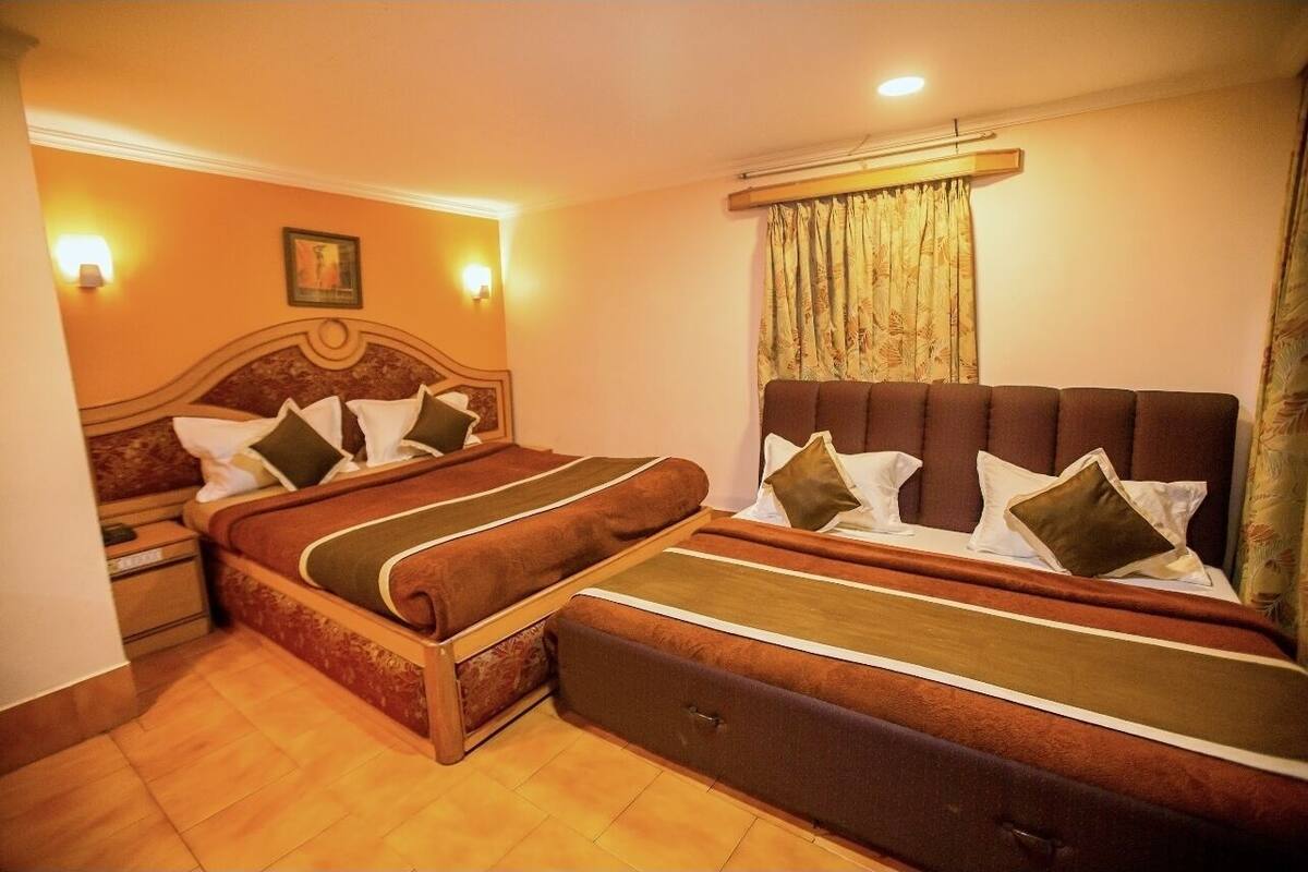 Un llit doble amb capçalera de fusta, dues taules de nit i una finestra gran amb cortines.