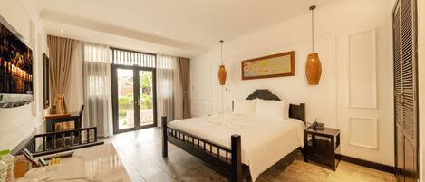 A hotel room with a bed, bedside table, and a desk with a chair. There is a window with curtains, a door, and a wall-mounted artwork.