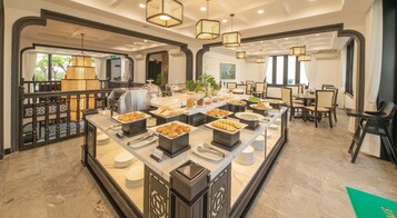 Montaje de bufé con diferentes opciones de comida, una estación de café y un área de estar con mesas y sillas.