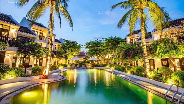 A resort with a swimming pool surrounded by palm trees and well-lit buildings. - Hoi An Coco River Resort & Spa (Da Nang)