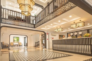 Un vestíbulo de hotel con mostrador de recepción, una escalera y un candelabro.
