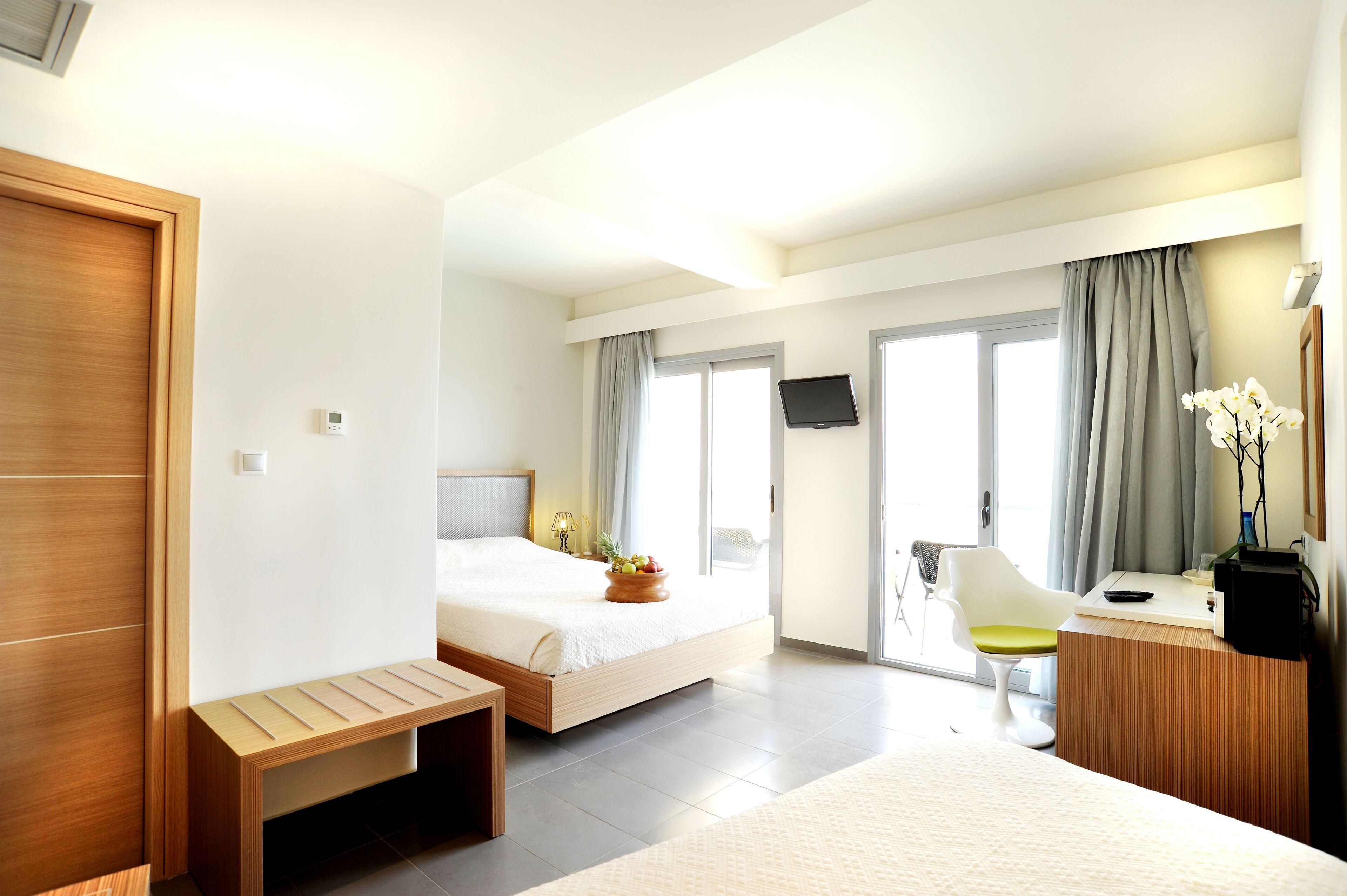 A modern hotel room with a bed, a desk, a chair, and a TV.