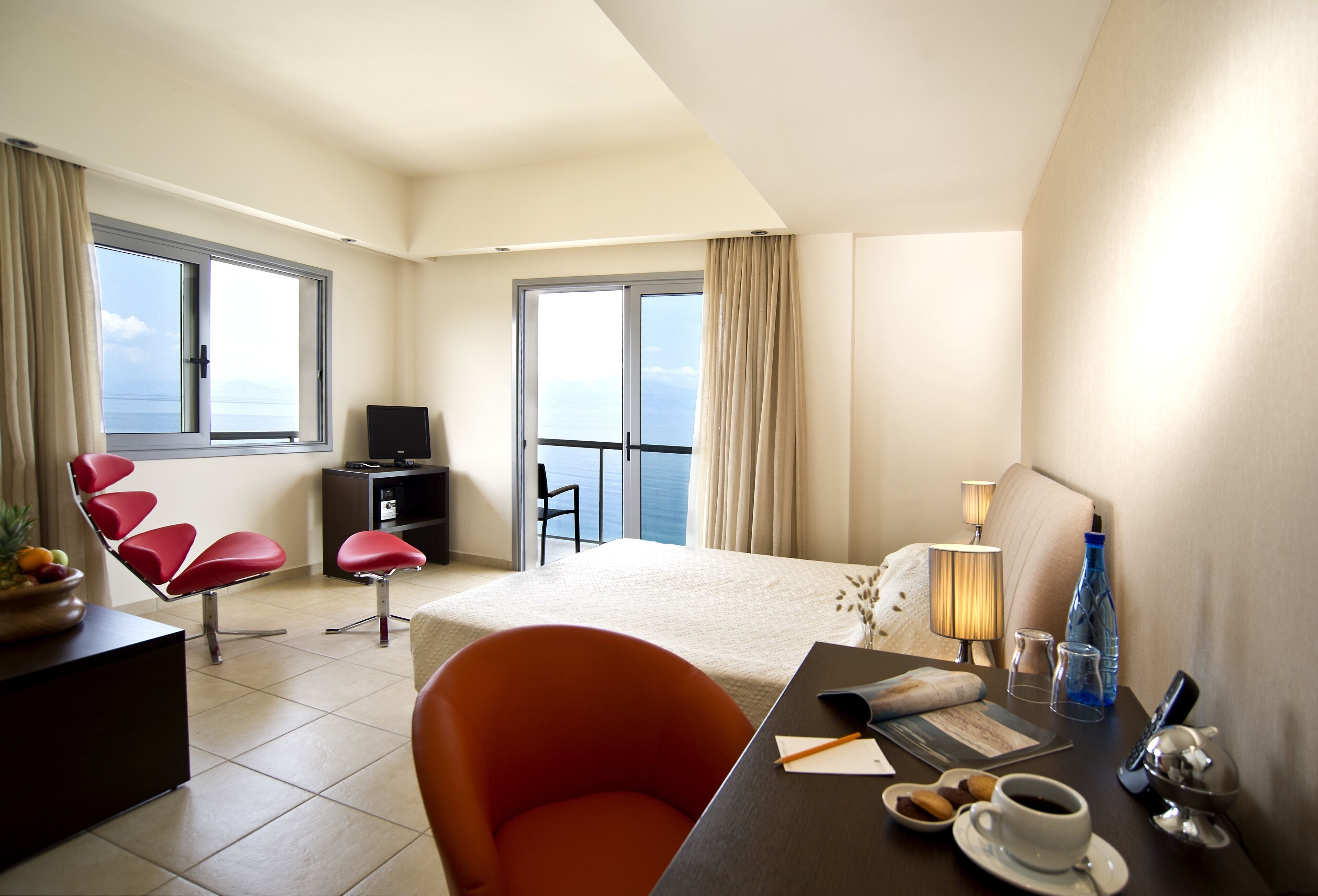 Ein Hotelzimmer mit Bett, Schreibtisch mit Stuhl, Fernseher, Balkon mit Sitzgelegenheit und Meerblick.