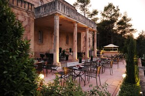 An outdoor patio with multiple tables and chairs, surrounded by columns and potted plants. - Sikyon Coast Hotel & Resort (Xylokastro-Evrostina)