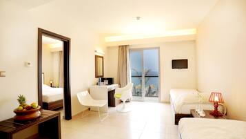 A hotel room with a bed, a desk, a chair, a television, and a view of the sea.