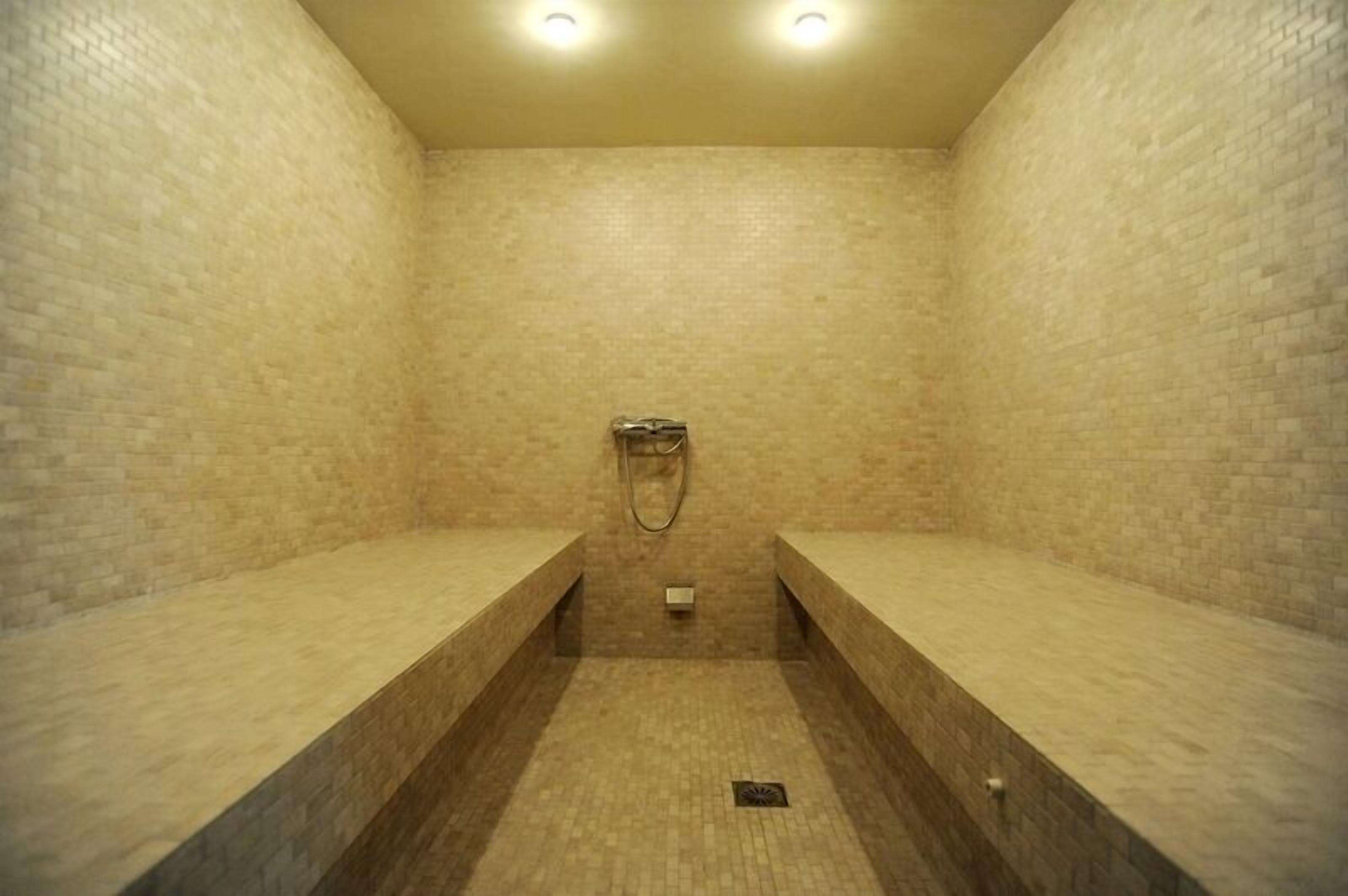 Une zone de douche carrelée, dotée de bancs et d’un pommeau de douche.