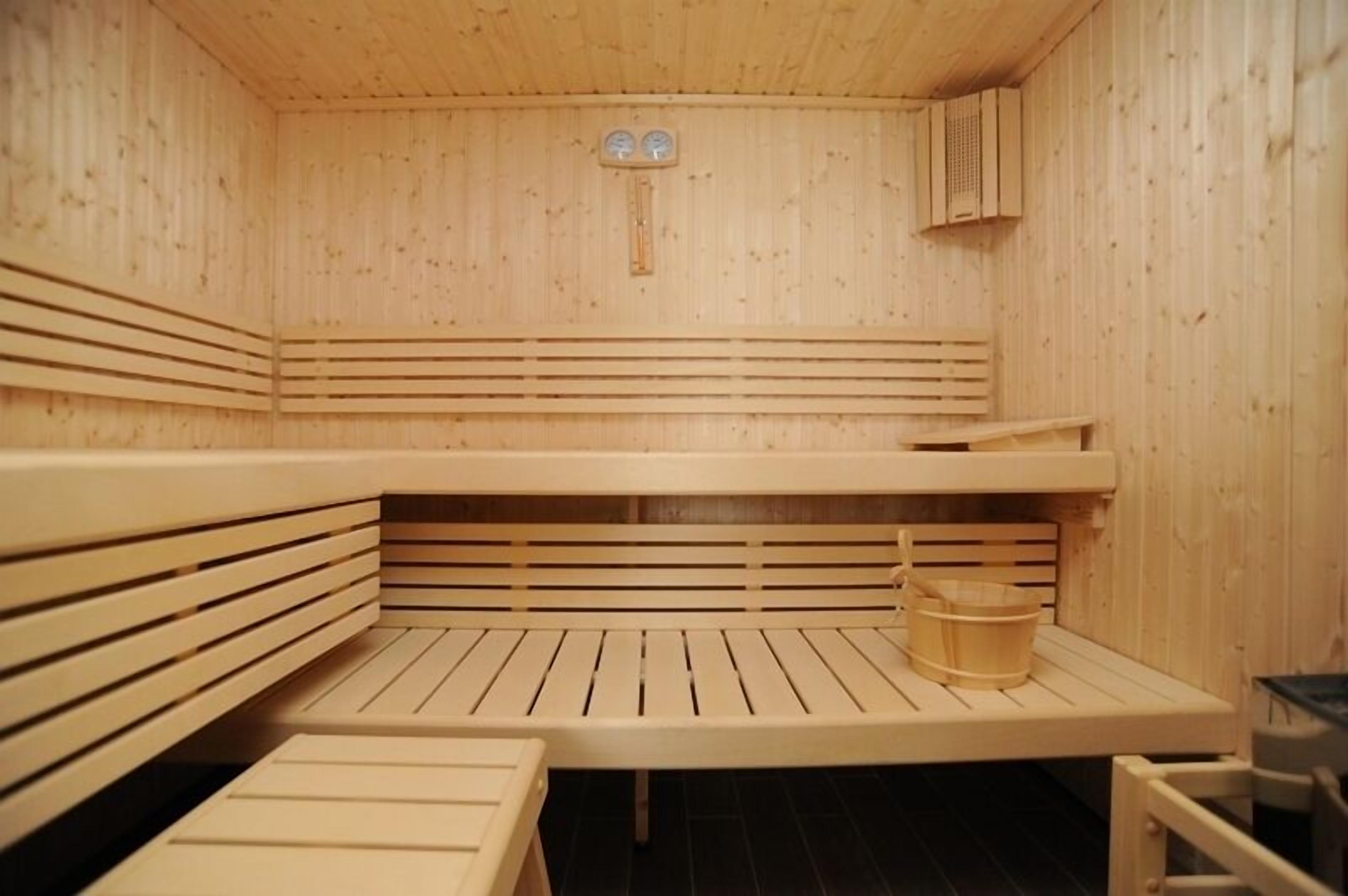 A sauna with wooden benches and a table, a bucket, and a thermometer on the wall.