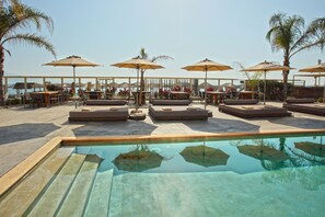 A poolside area with lounge chairs and umbrellas, a clear pool, and a view of the sea. - Sikyon Coast Hotel & Resort (Xylokastro-Evrostina)