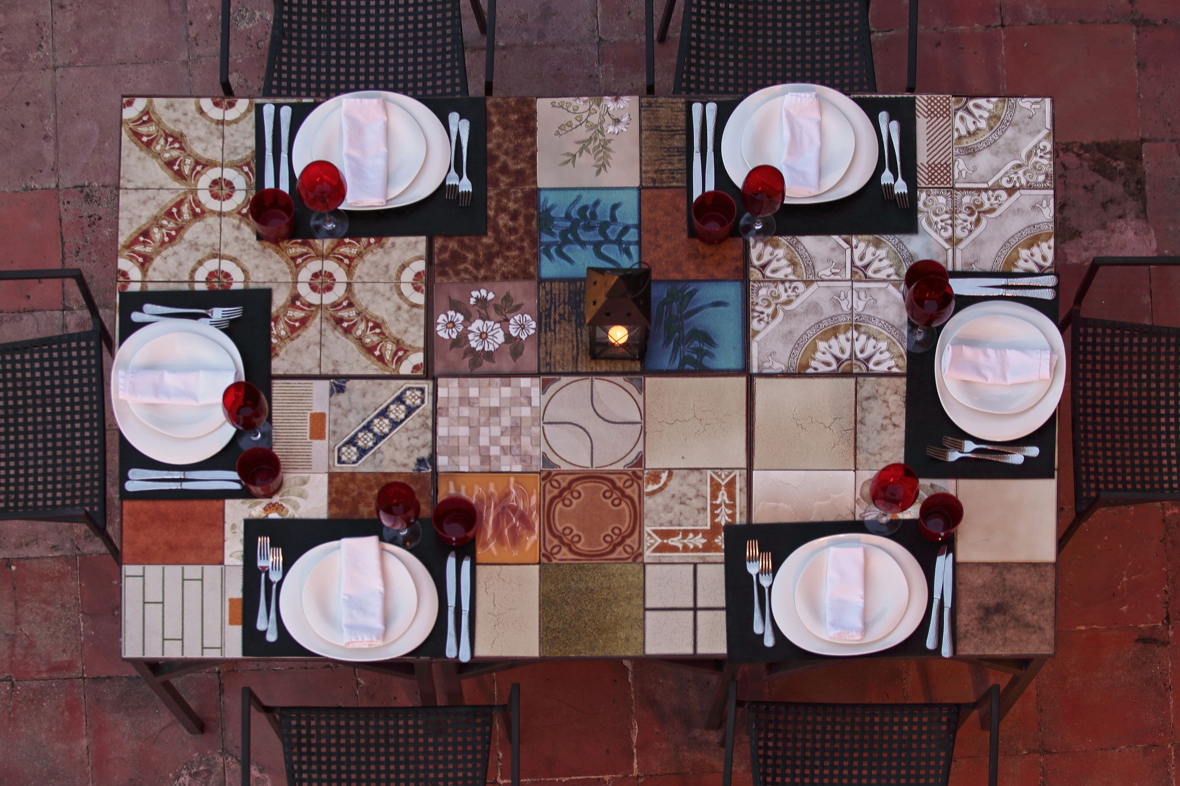 A dining table set for four with a mosaic tile design, black chairs, and red wine glasses.