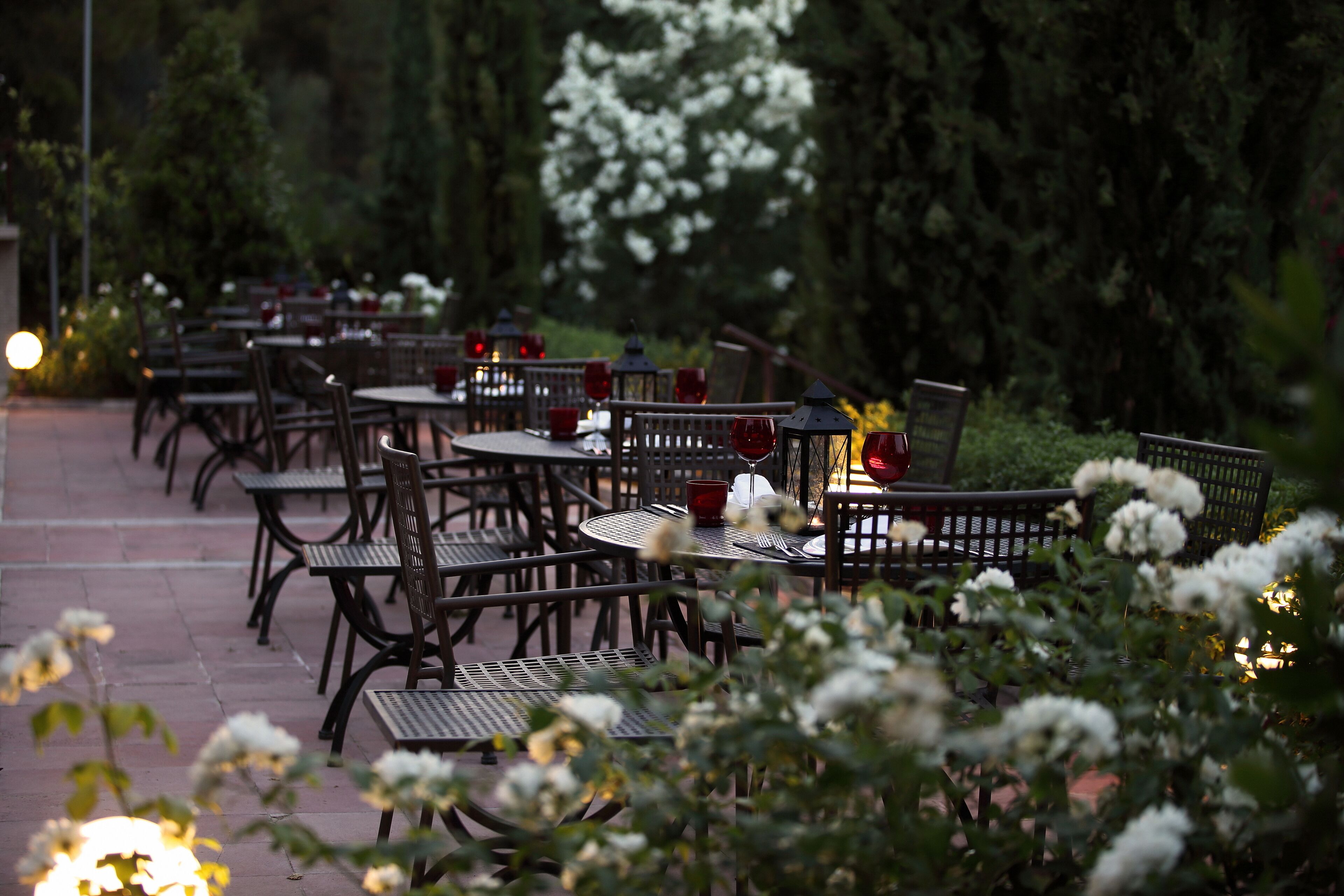 An outdoor dining area with tables and chairs, surrounded by greenery and flowers.