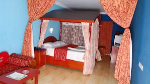 A four-poster bed with a canopy, a bedside table with a lamp, and a red sofa in a room with blue walls. - Apple Valley (Kodaikanal)