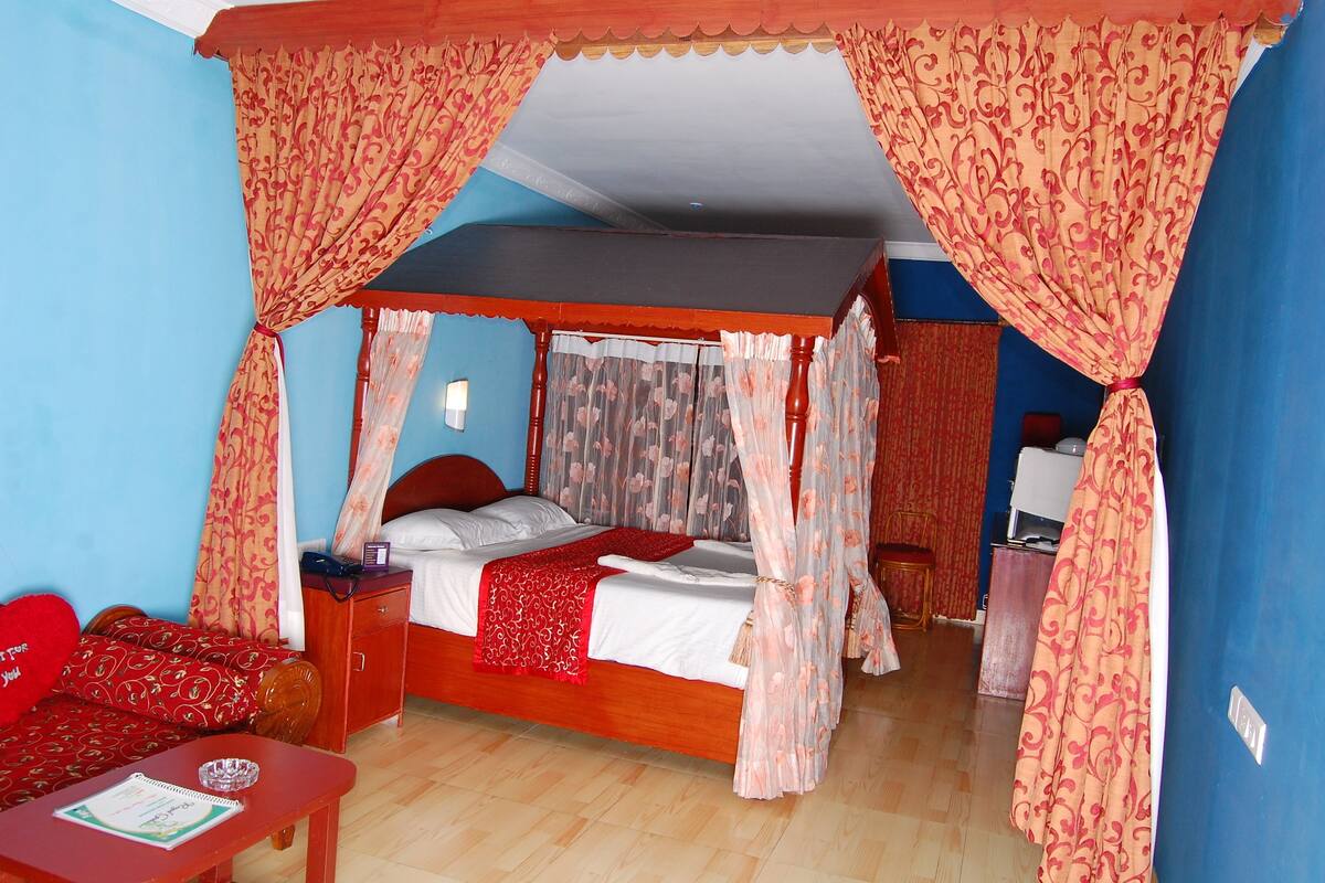 A four-poster bed with a canopy, a bedside table with a lamp, and a red sofa in a room with blue walls.