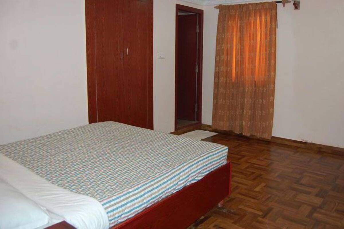 A bedroom with a bed, wooden wardrobe, and a door leading to another room.
