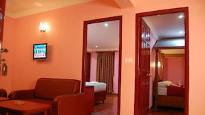 A hotel room with a red sofa, a small table, a TV on the wall, a bed with a red blanket, and a wooden door. - Apple Valley (Kodaikanal)