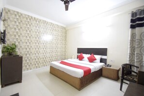 Un dormitorio con cama, mesita de noche, una silla y una planta.