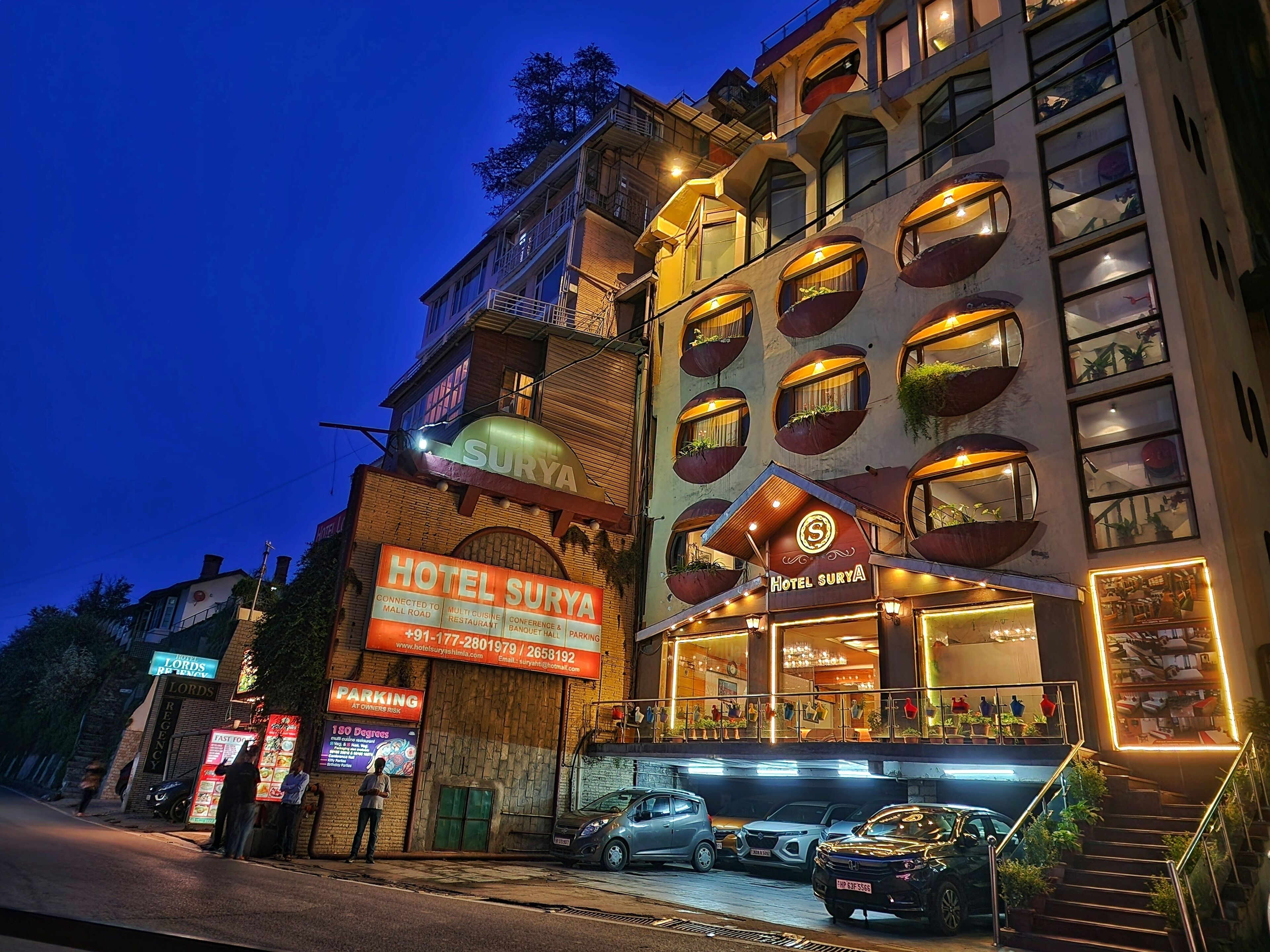 A hotel with a sign reading "HOTEL SURYA," connected to a mall, and featuring a multi-cuisine restaurant.