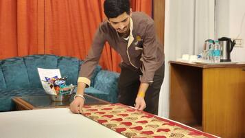 Una persona preparando una cama con una colcha estampada en una habitación con un sofá azul y una mesita de madera.