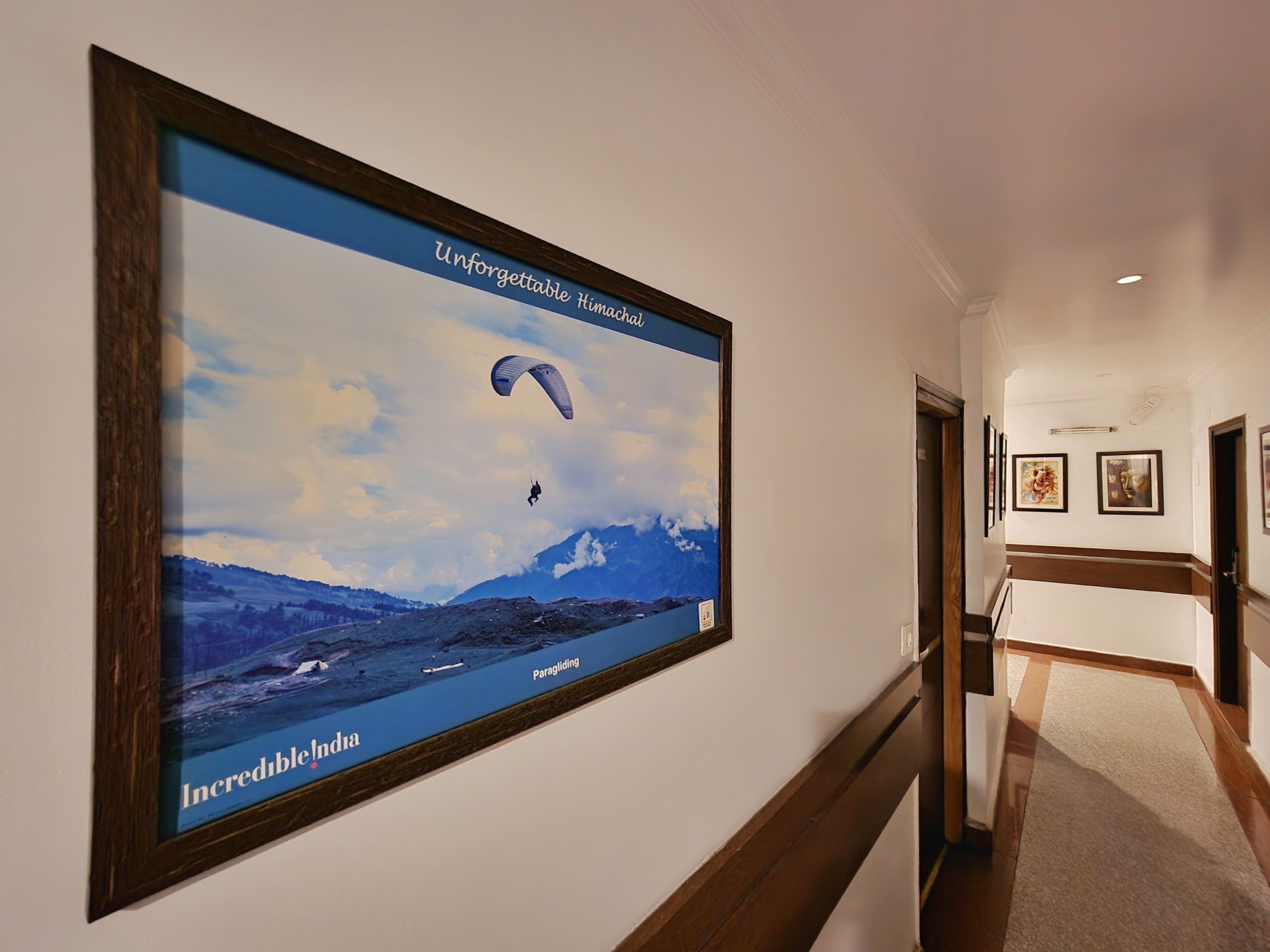 A hallway with a large framed poster of a paragliding scene over India, labeled "Incredible! India".