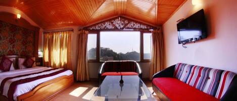 A room with a bed, a sofa, a glass-top table, and a TV mounted on the wall.