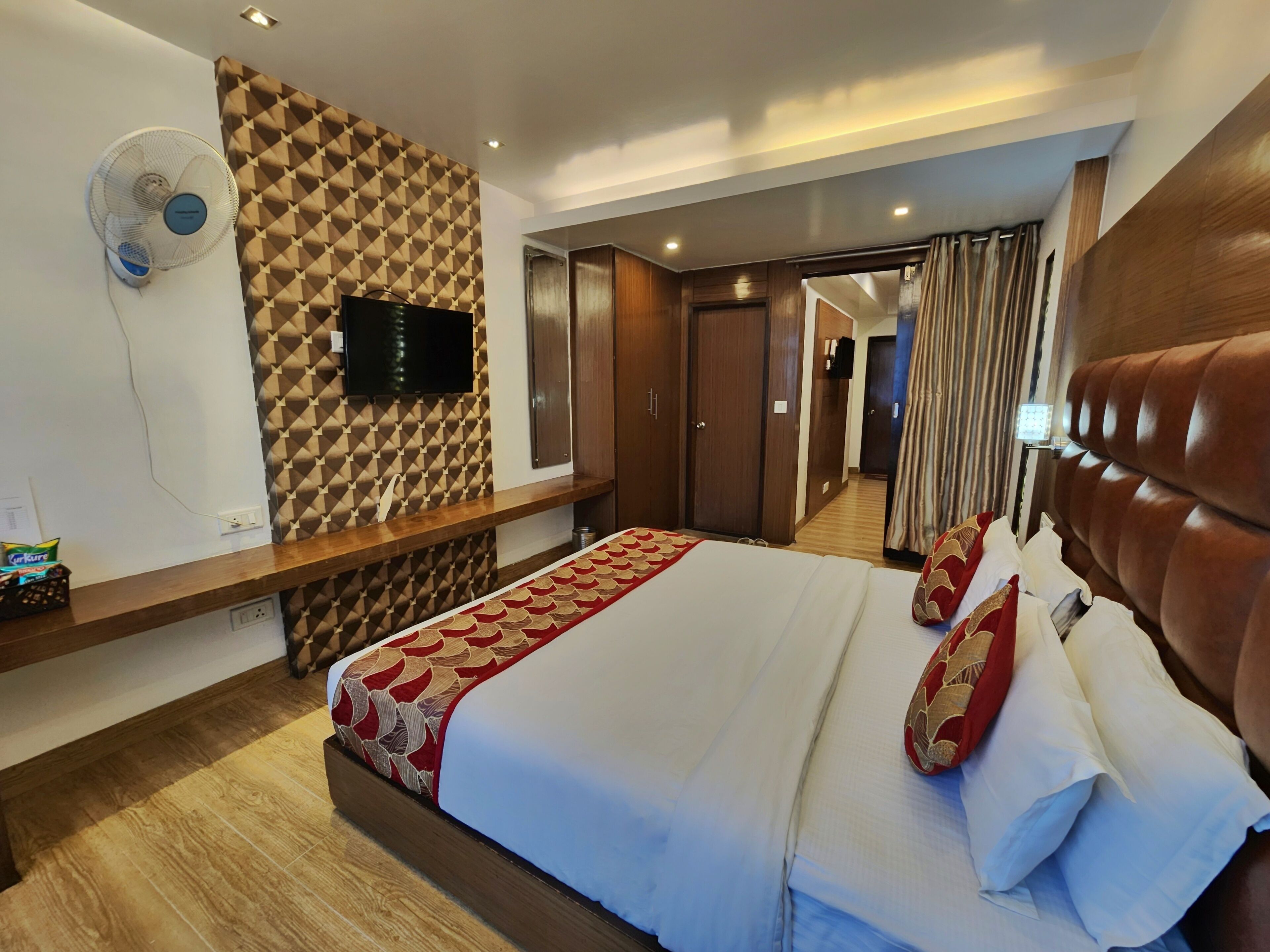 A hotel room with a large bed, a TV mounted on the wall, a built-in fan, and a wooden headboard.