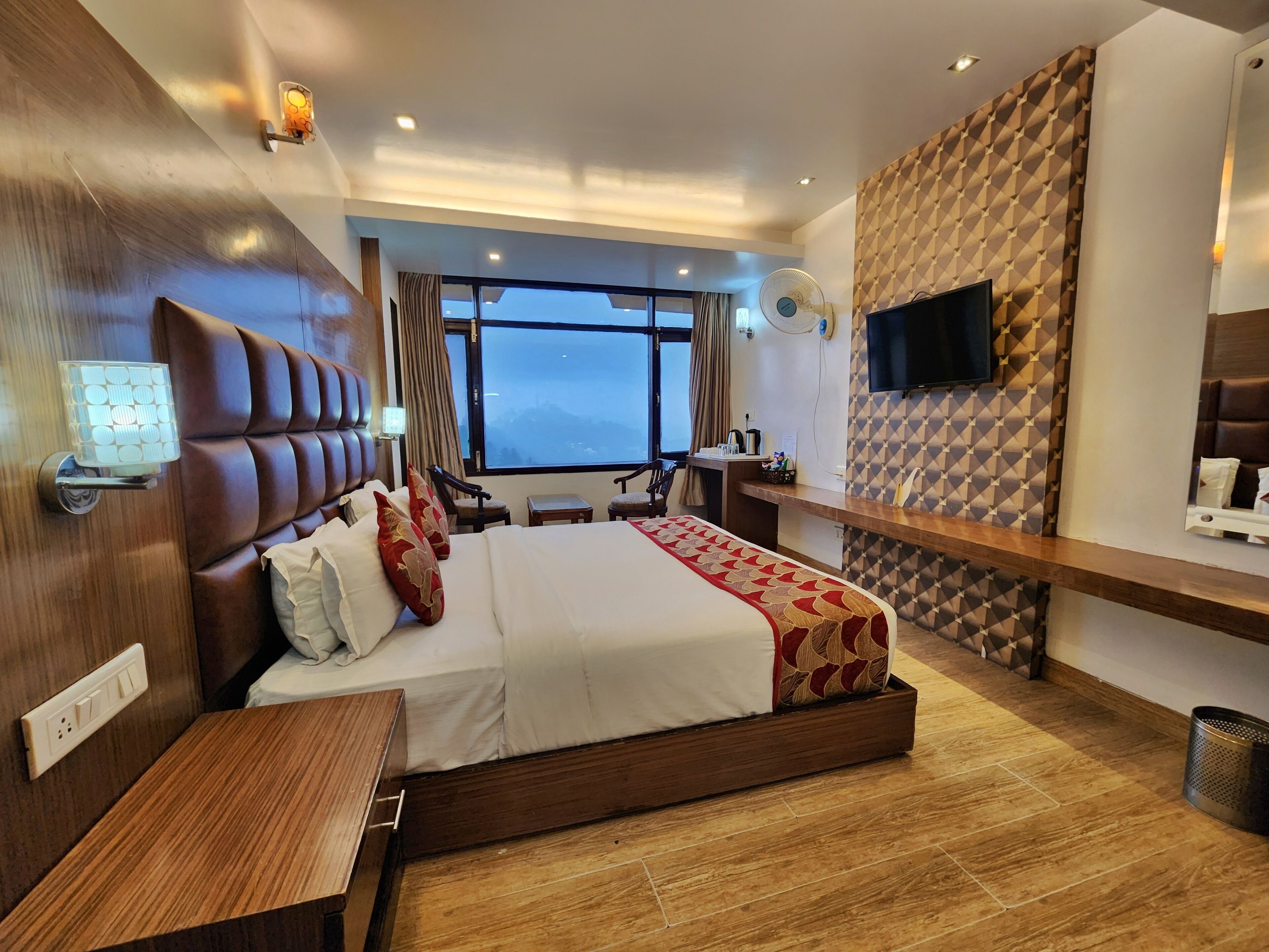 Een moderne hotelkamer met een groot bed, een bureau, een televisie en uitzicht op de bergen.