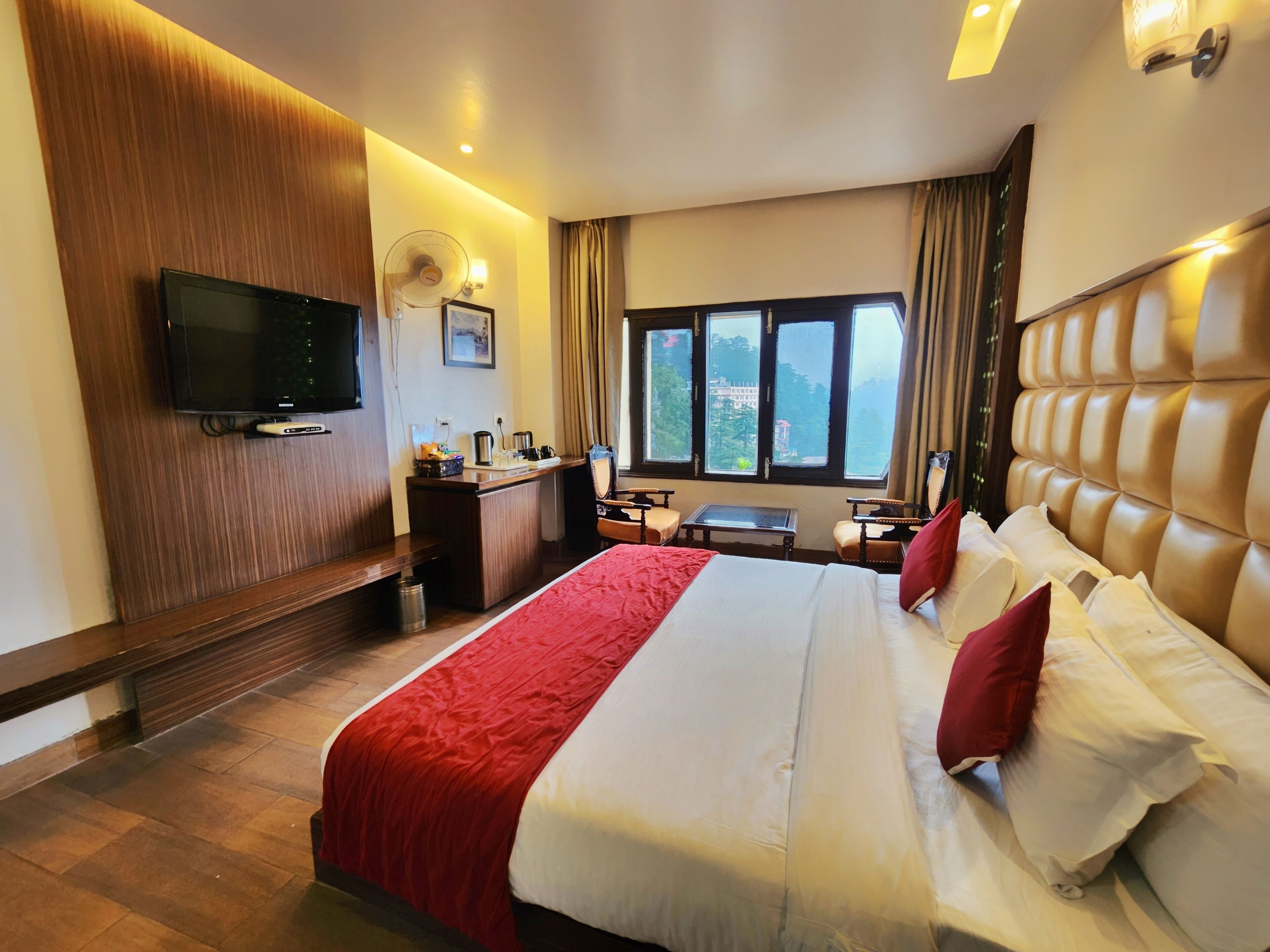 Quarto de hotel com cama, escrivaninha, televisão e janela com vista.
