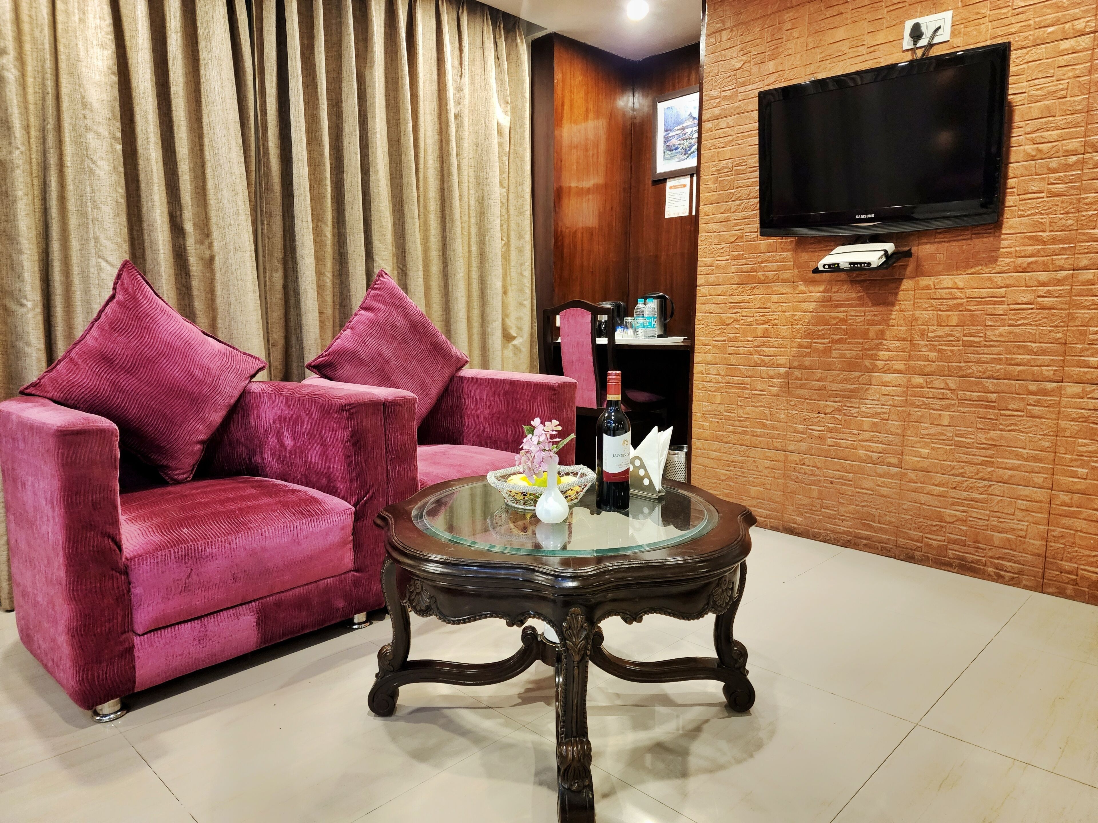 A living room with a pink sofa, a glass coffee table, and a flat-screen TV mounted on a brick wall.
