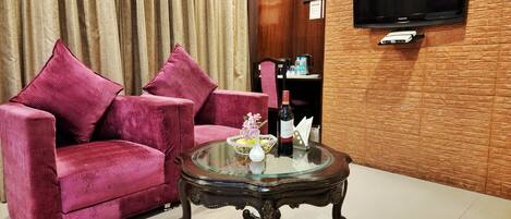 A living room with a pink sofa, a glass coffee table, and a flat-screen TV mounted on a brick wall.