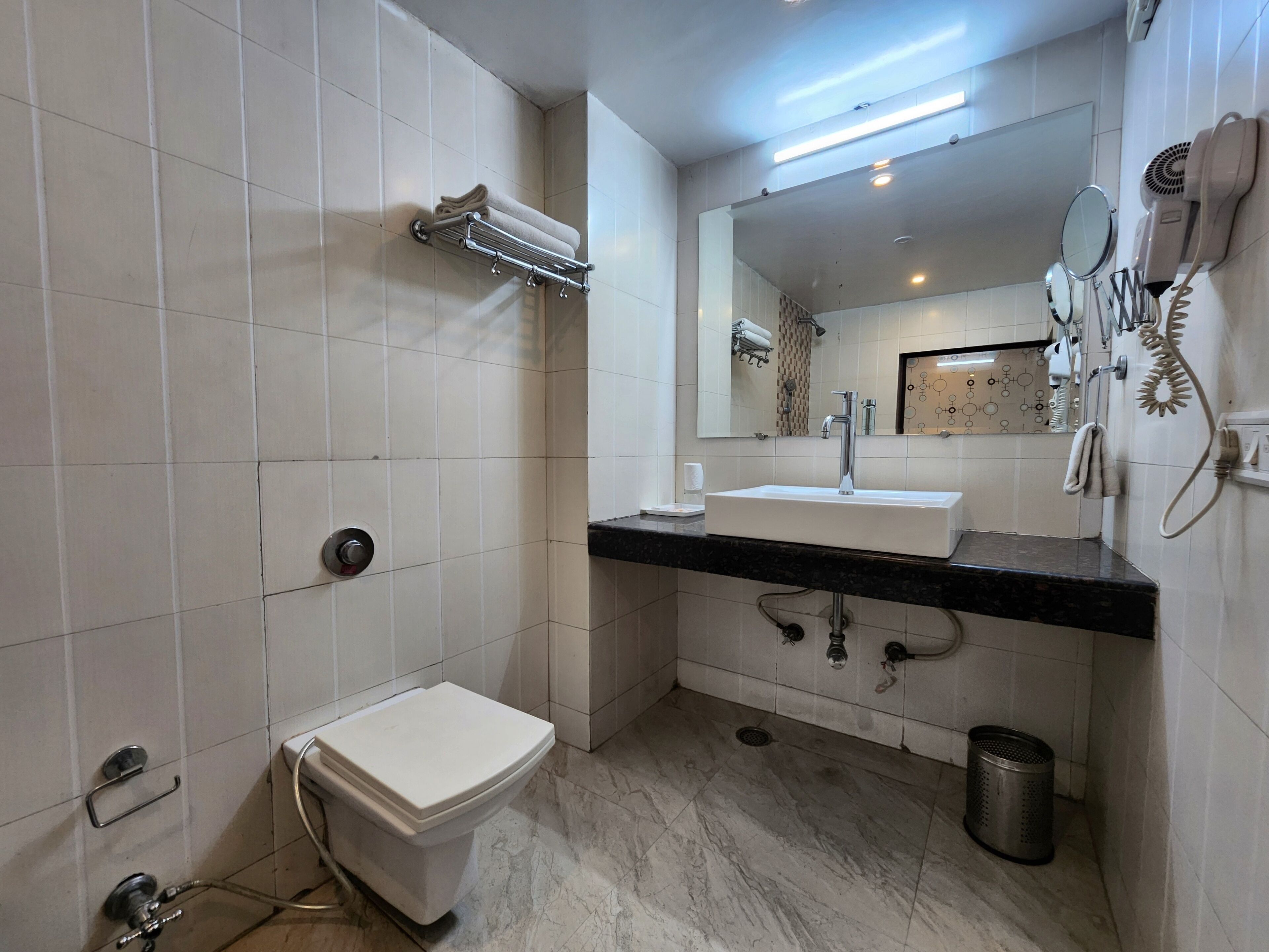 Et moderne badeværelse med et hvidt toilet, en vask med spejl og en håndklædestang.