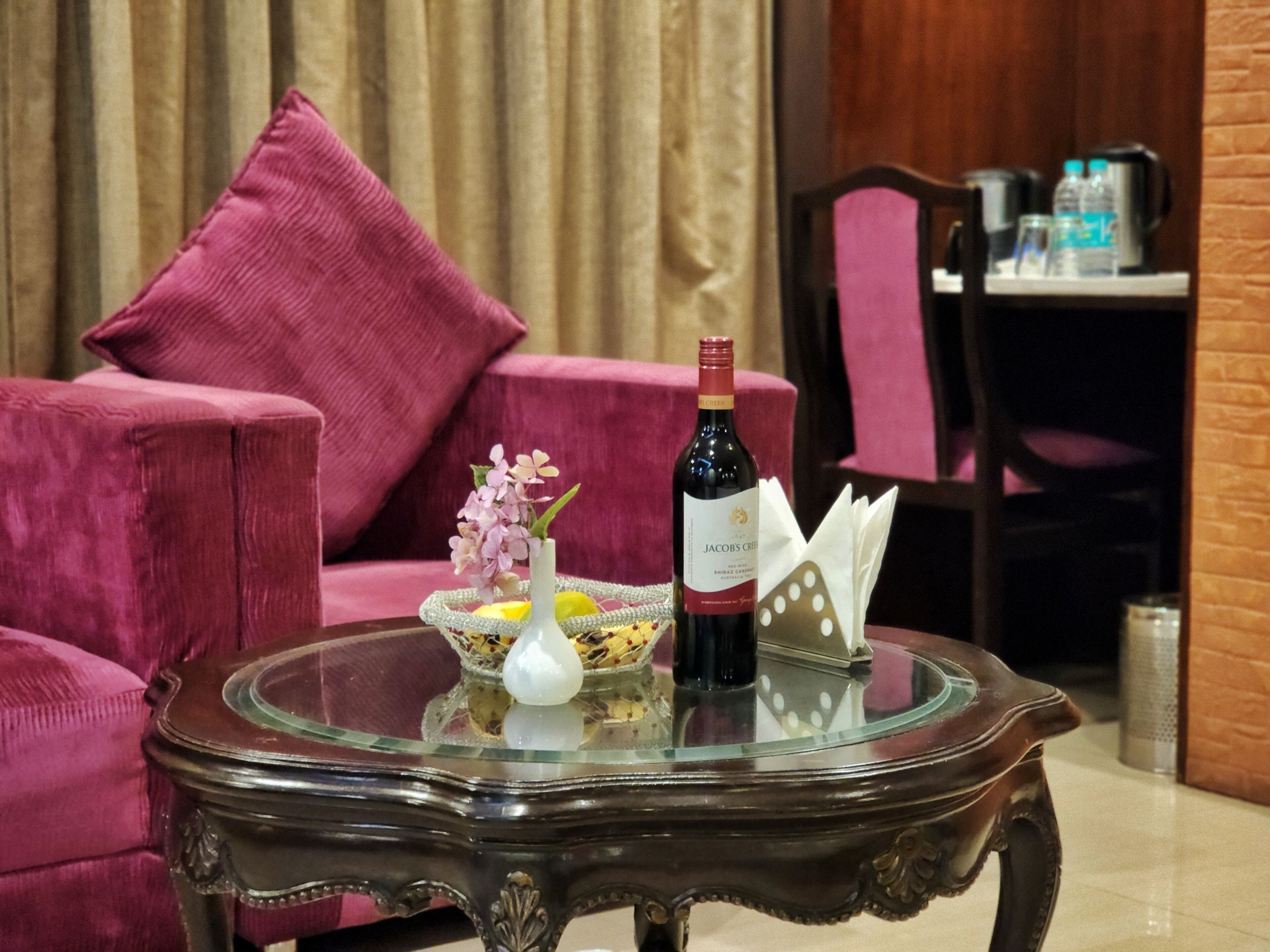 A glass table with a bottle of wine, a vase with flowers, and a bowl of fruit.