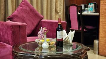 Una mesa de vidrio con una botella de vino, un florero con flores y un cuenco de fruta.