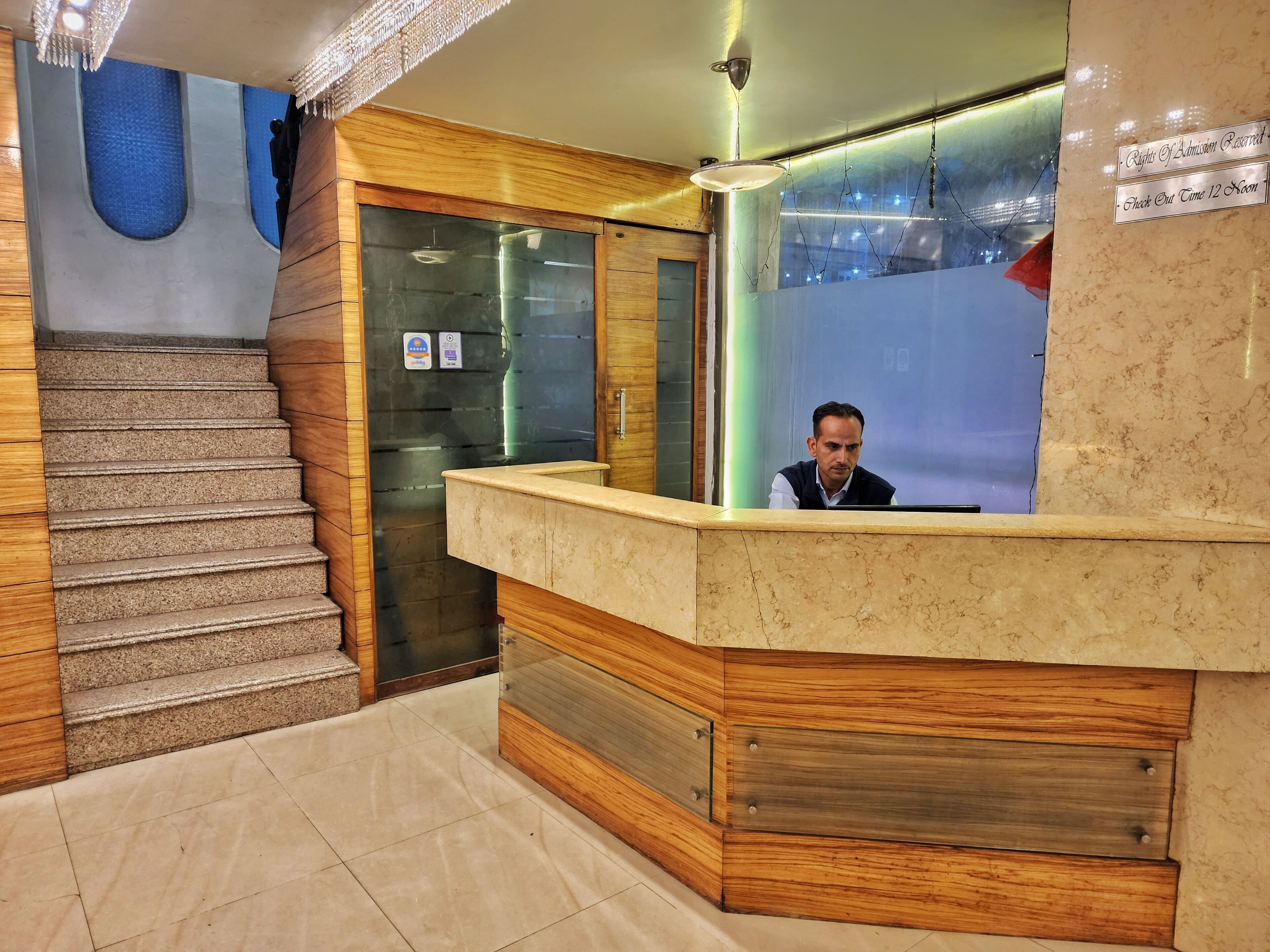 A hotel reception area with a marble counter, wooden paneling, and a glass elevator.
