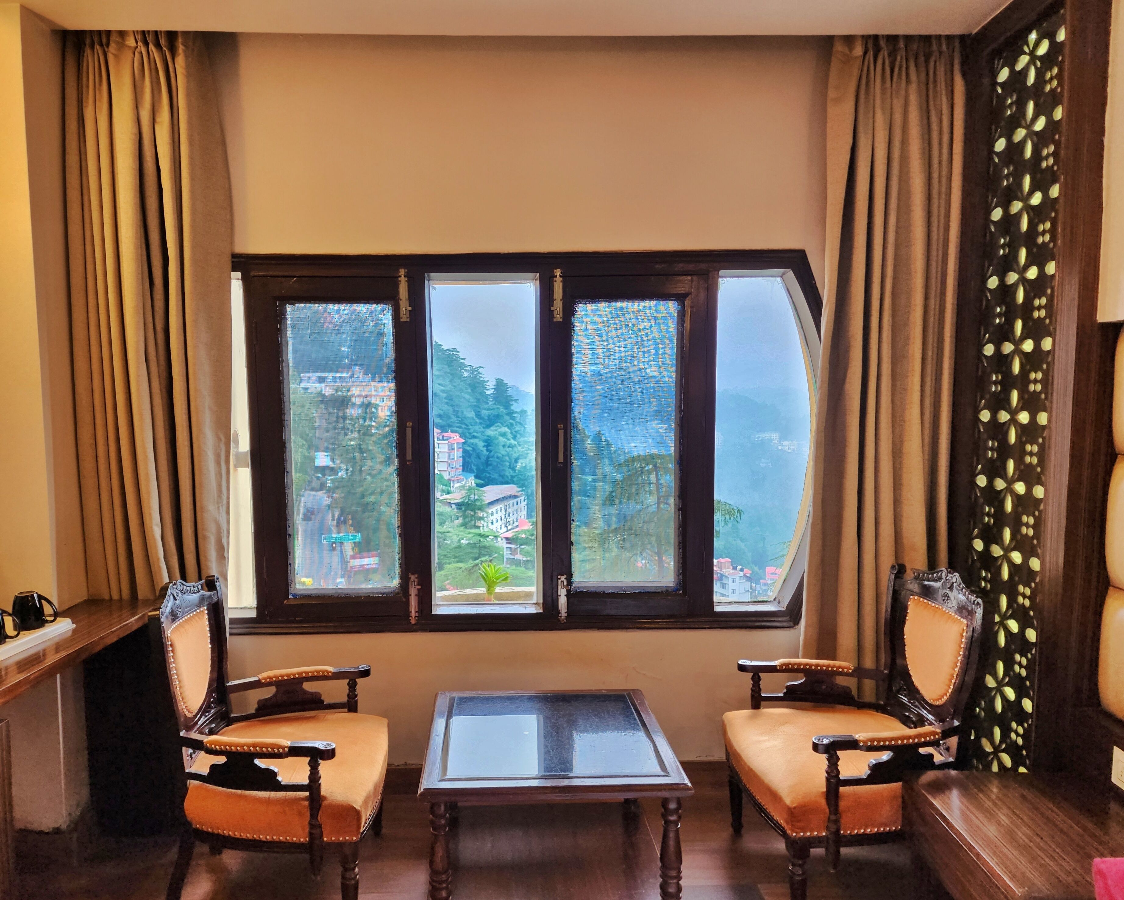 A room with a large window offering a view of a mountainous landscape. There are two wooden chairs and a small table in the room.
