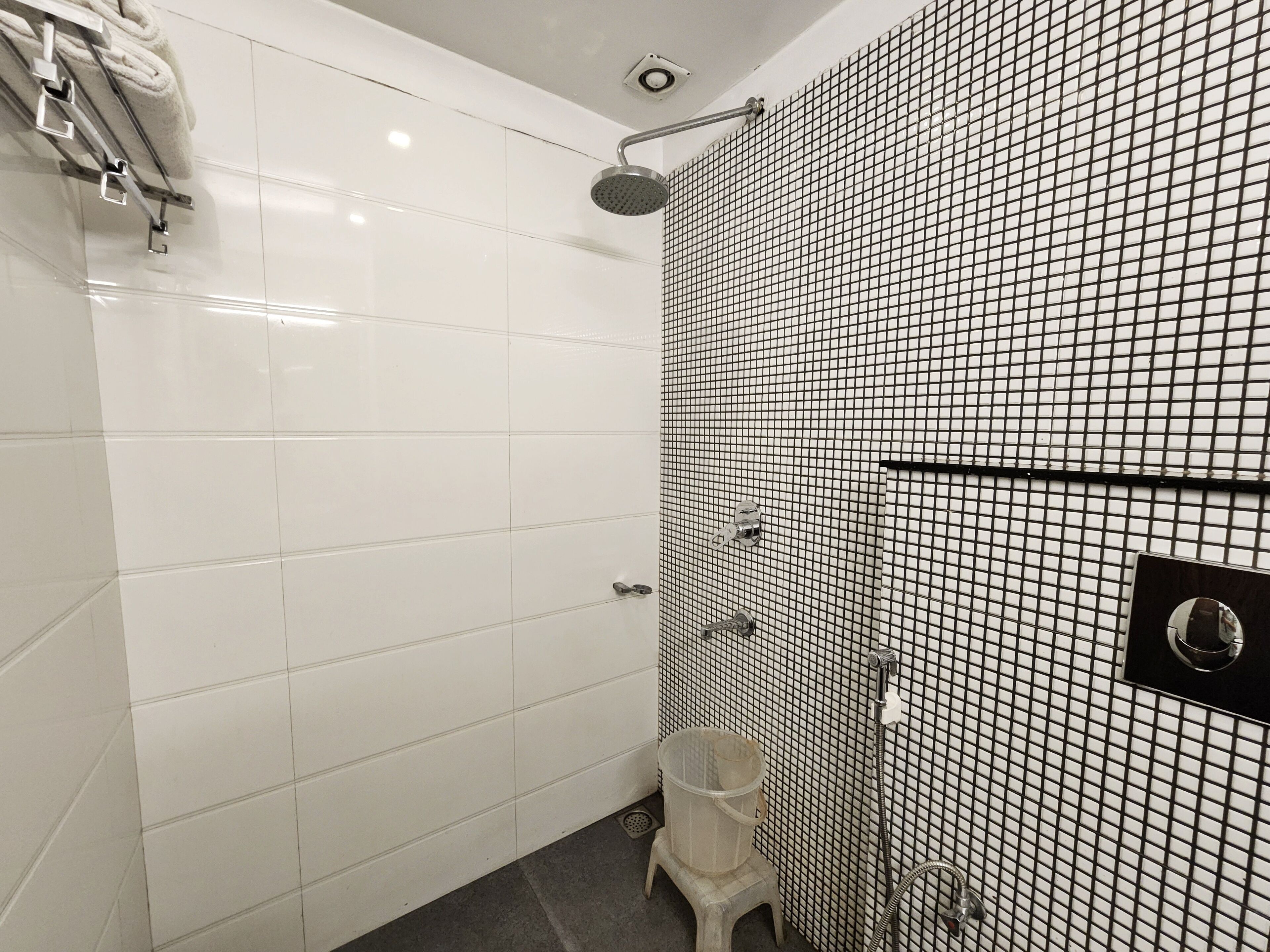 A modern bathroom with white tiles, a shower with a grid-patterned wall, and a small trash bin.