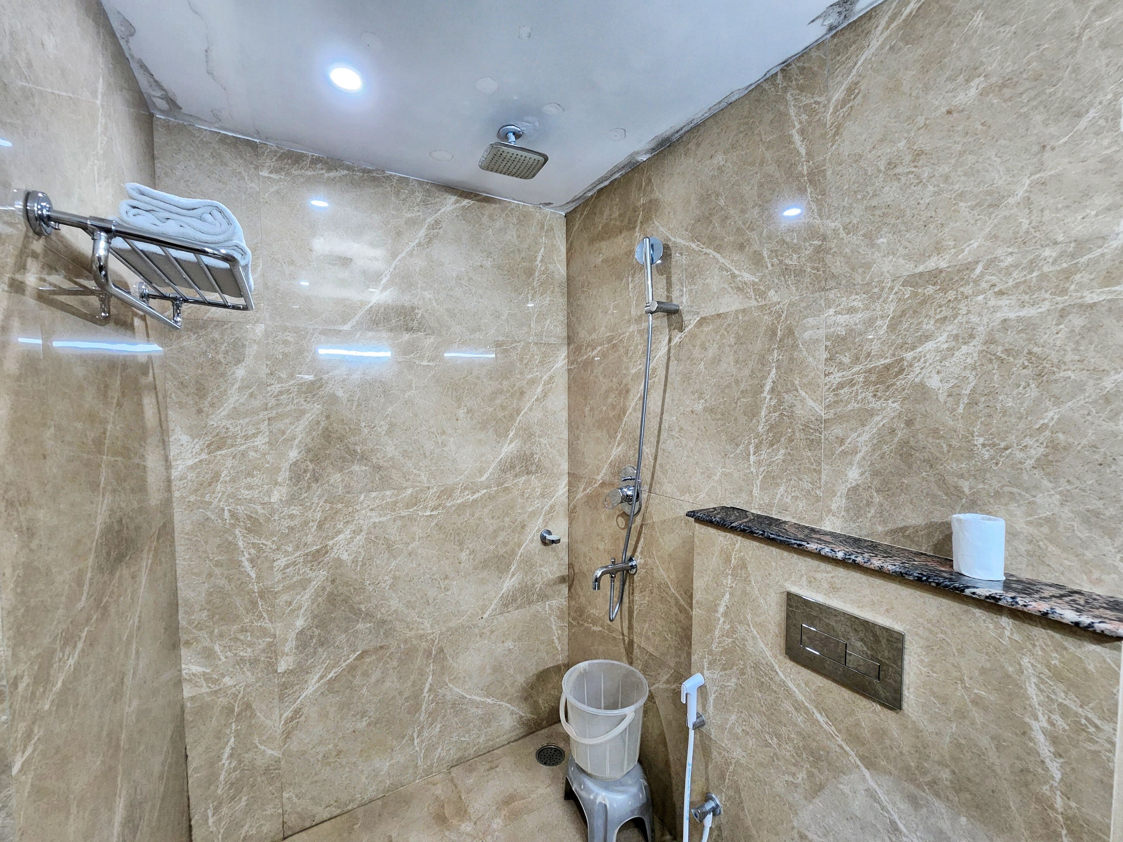 Een badkamer met een marmeren vloer, een douche, een handdoekhouder, een toilet en een plankje met een toiletrol.