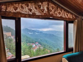 Una habitación con un ventanal grande que da a un paisaje montañoso y un pueblo pequeño abajo.