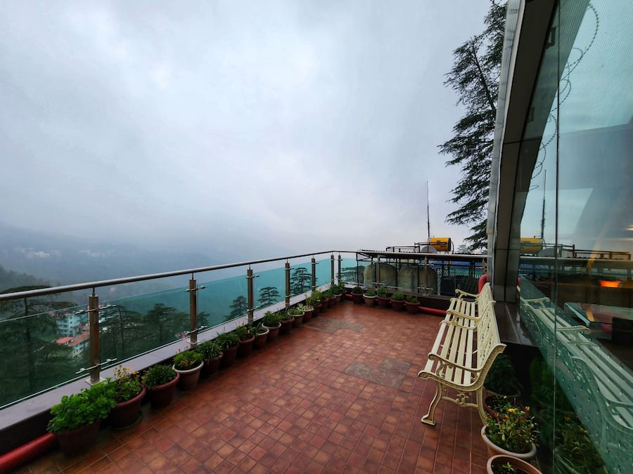 Un balcon agrémenté de plantes en pot, d’un banc et offrant une vue sur un paysage montagneux.
