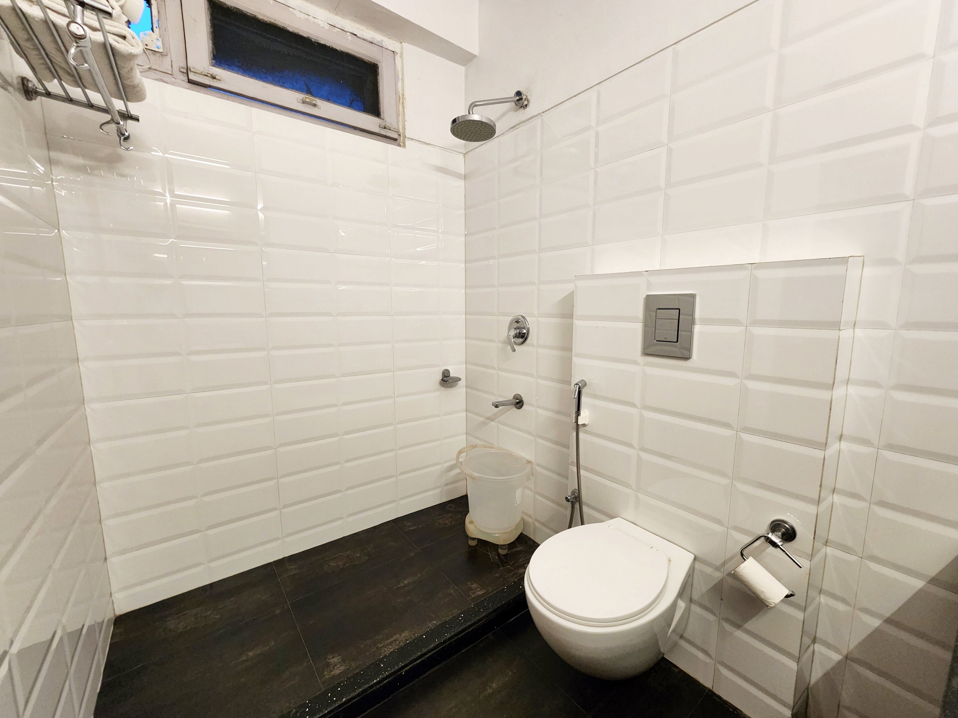 A small, modern bathroom with white subway tiles, a black floor, a toilet, a shower, and a towel rack.