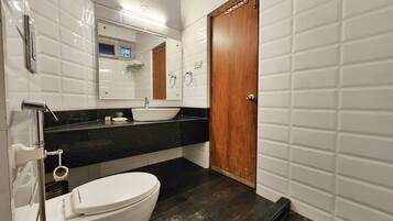 A modern bathroom with a white toilet, black countertop, and a wooden door.
