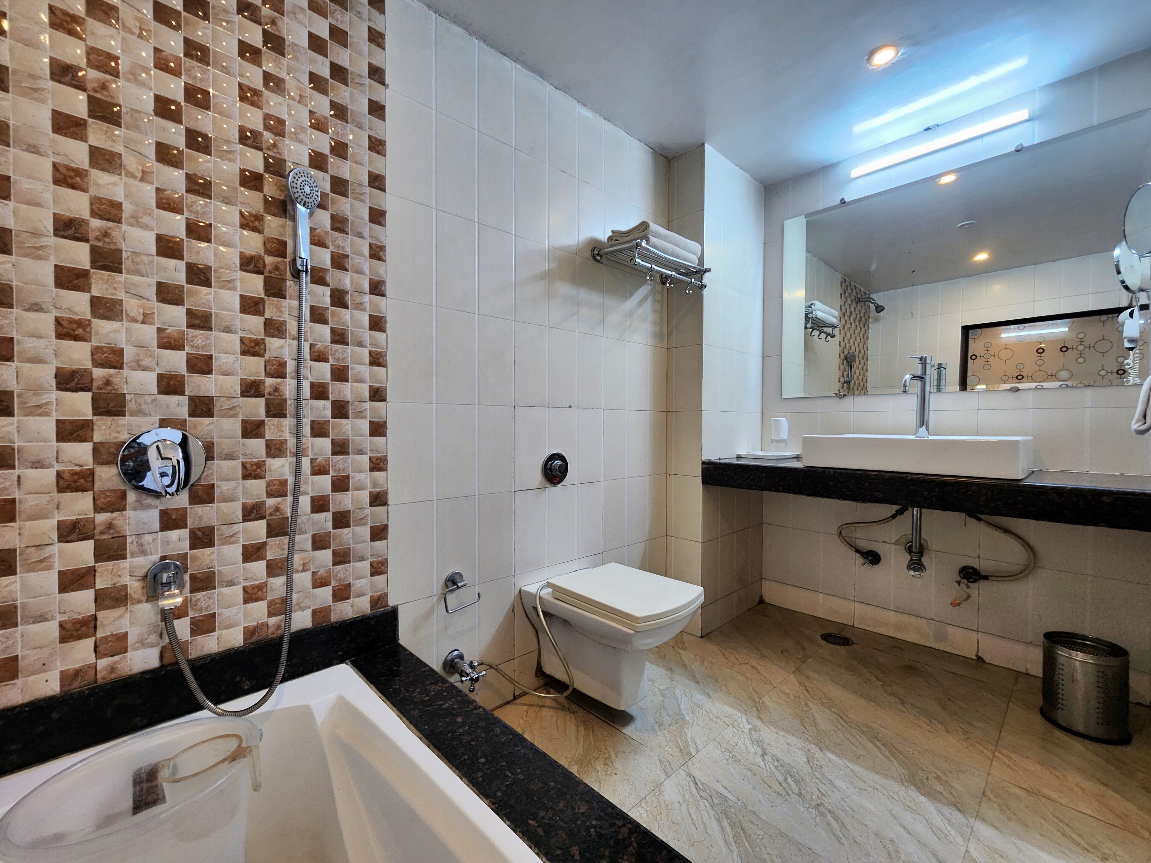 A modern bathroom with a checkered tile backsplash, a white toilet, a bathtub, a sink, and a mirror.