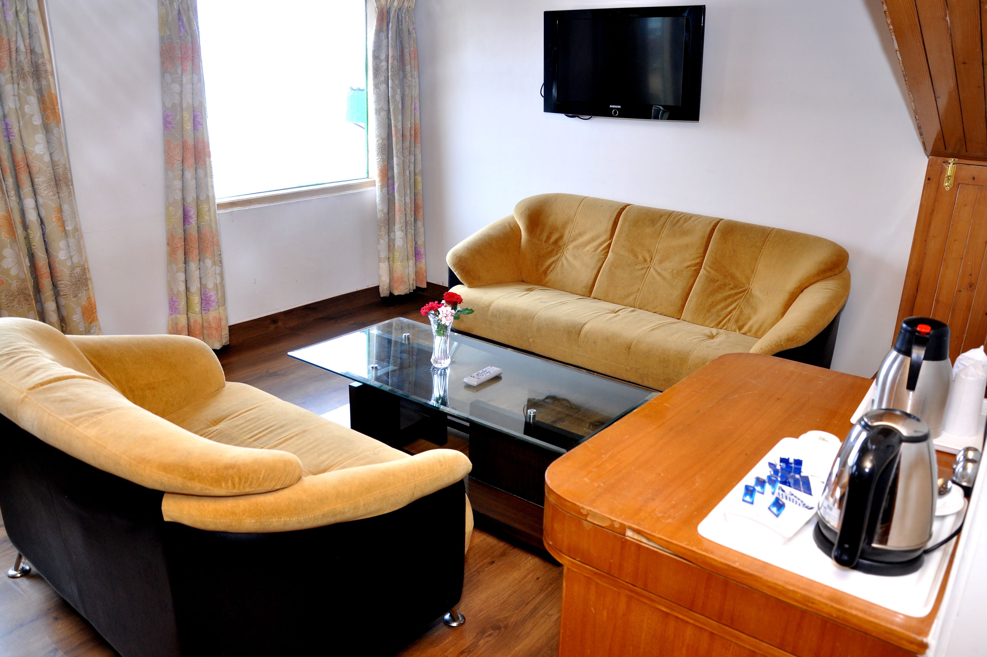 A living room with a sofa, a coffee table, a TV mounted on the wall, and a window with curtains.