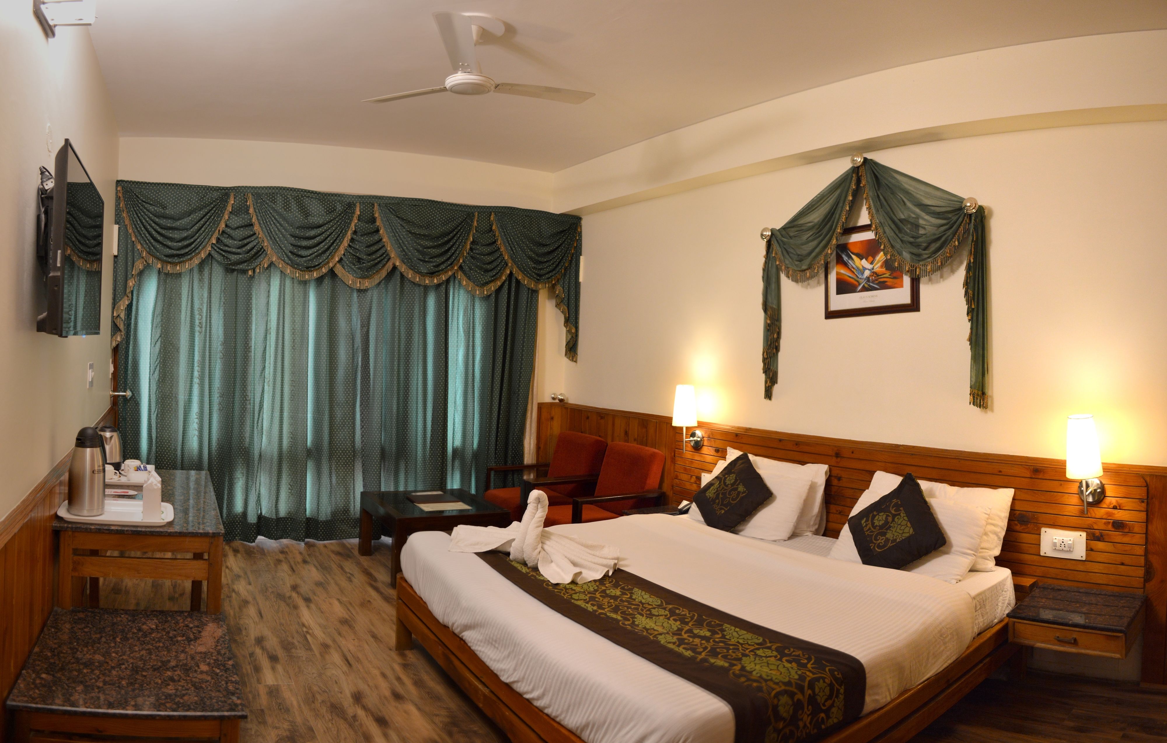 A hotel room with a bed, bedside lamps, a desk with a coffee maker, a chair, and a TV.