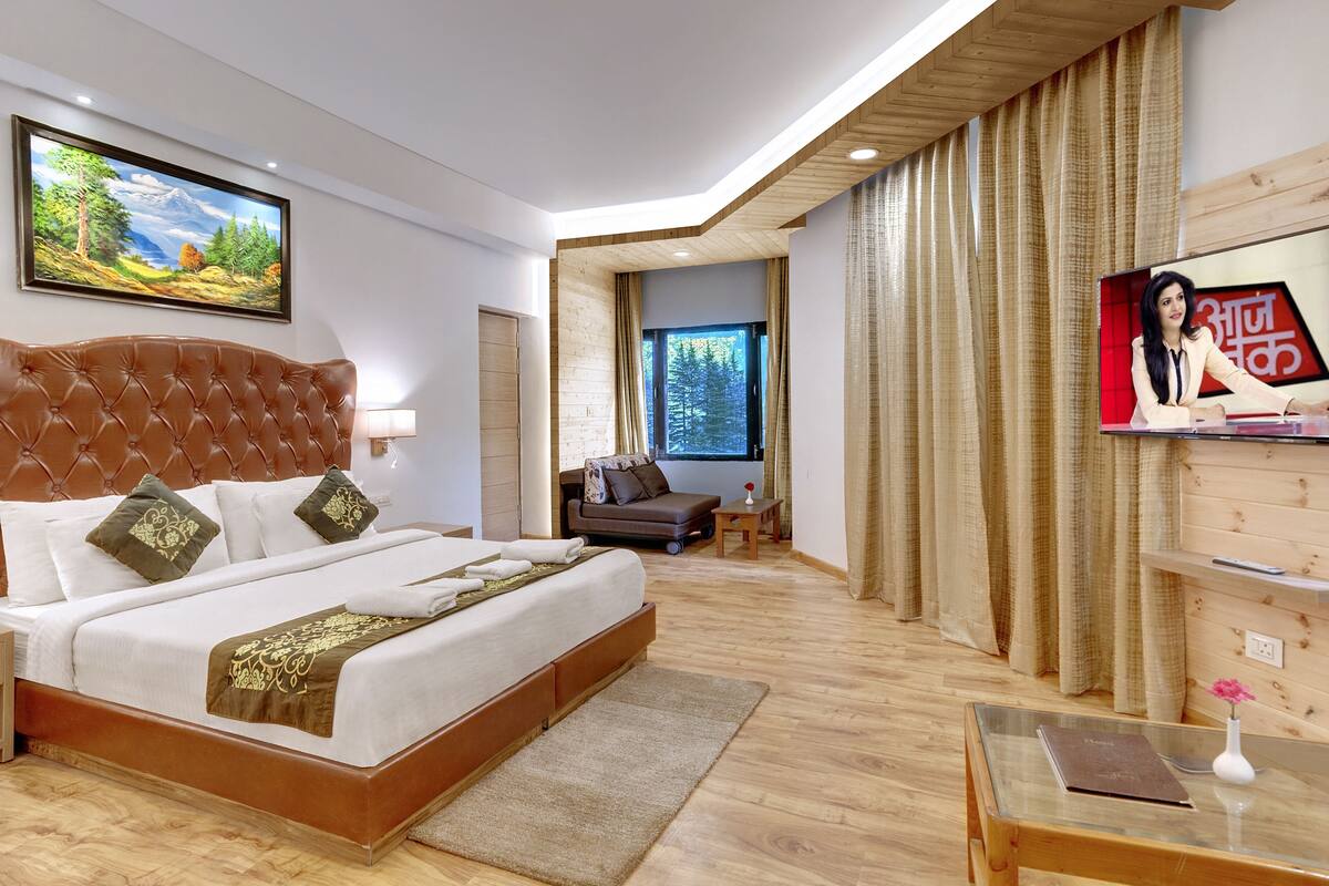 A modern hotel room with a large bed, a TV, and a view of a forest through a window.