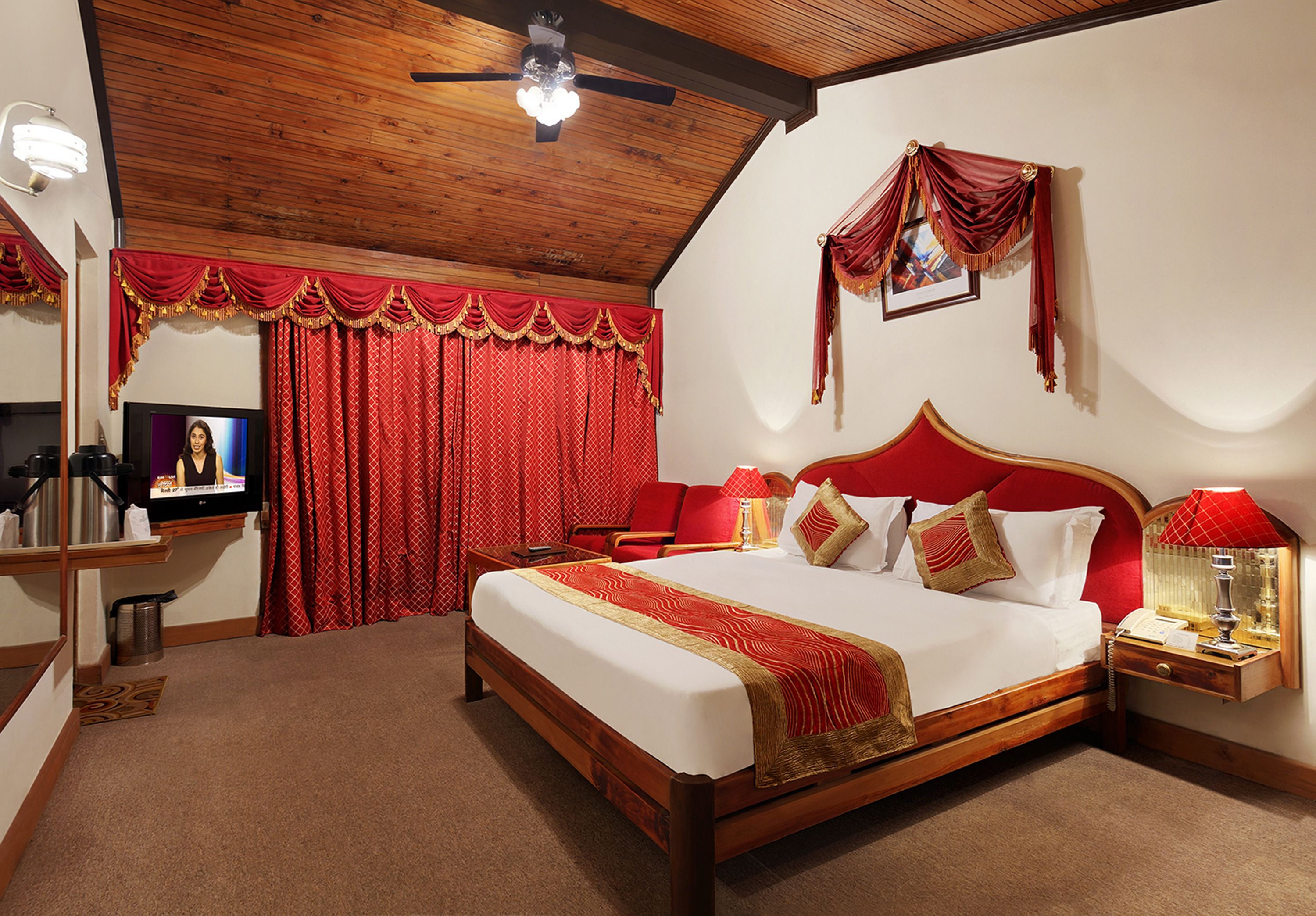 A hotel room with a large bed, a TV, a desk, and a red curtain.