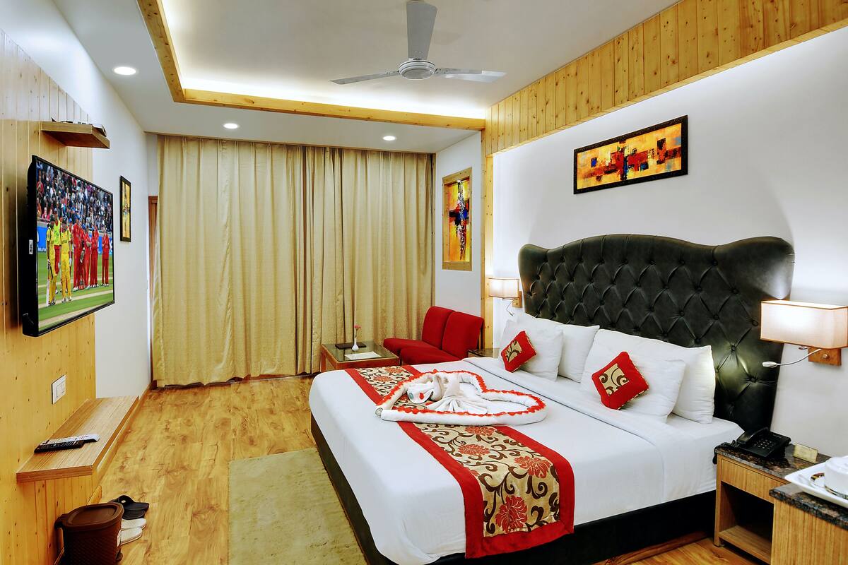 A hotel room with a large bed, a red armchair, a television, and a painting on the wall.