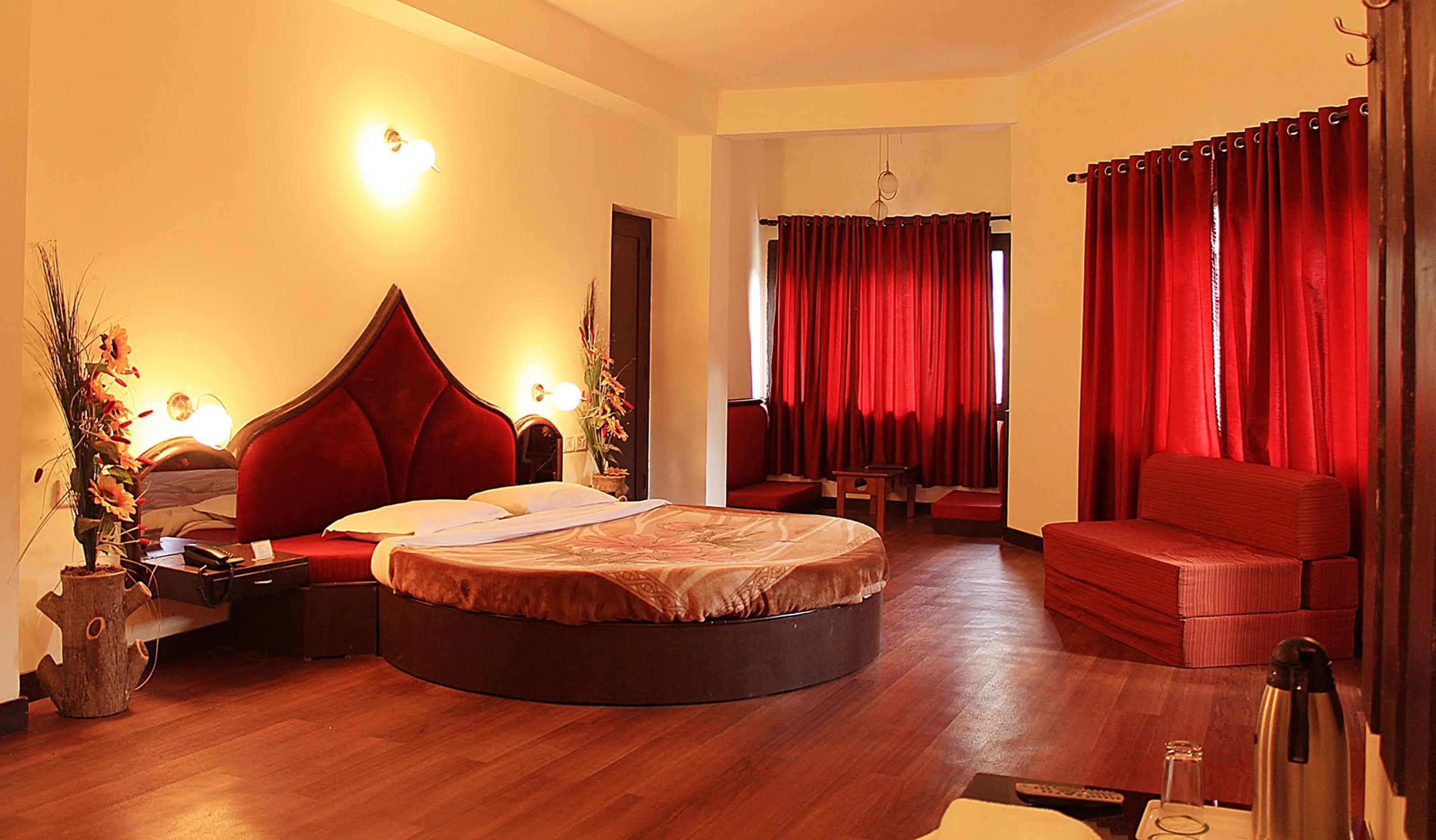 A hotel room with a round bed, a sofa, a small table, and a TV.