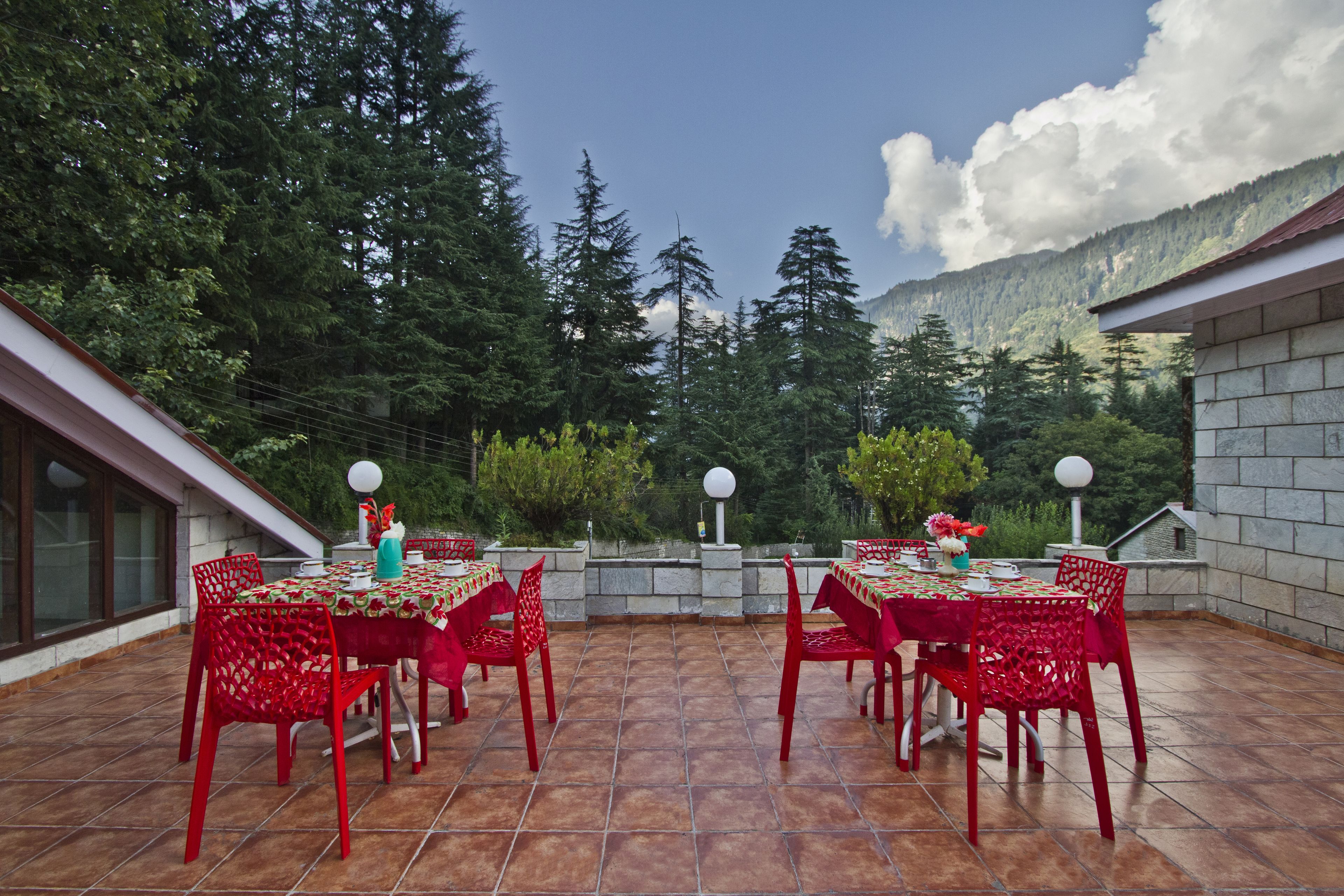A patio with red chairs and tables, surrounded by stone walls and a view of a forested mountain range.